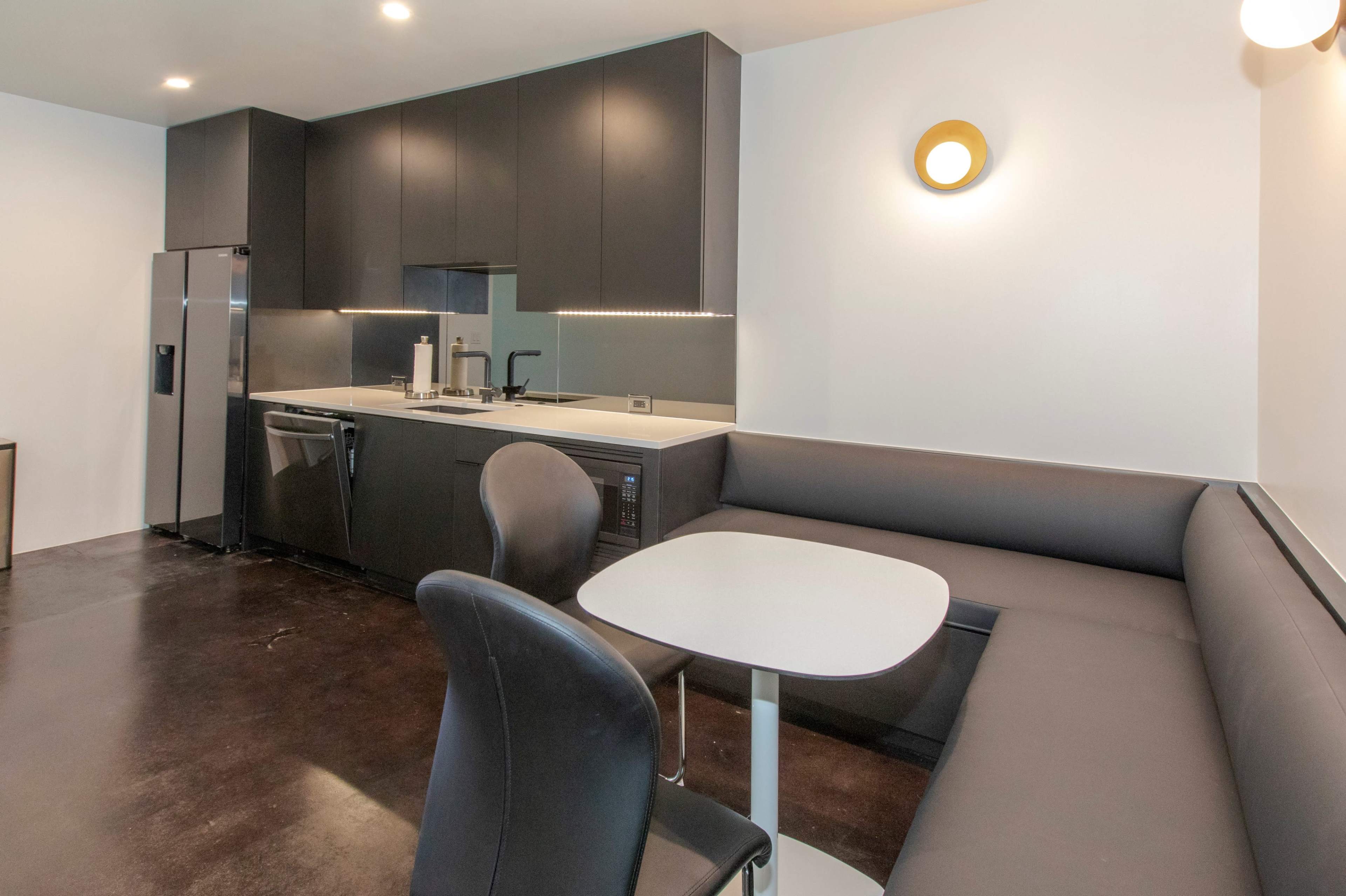 A modern kitchen features dark cabinetry, stainless steel appliances, and a sleek table with a bench seating area.