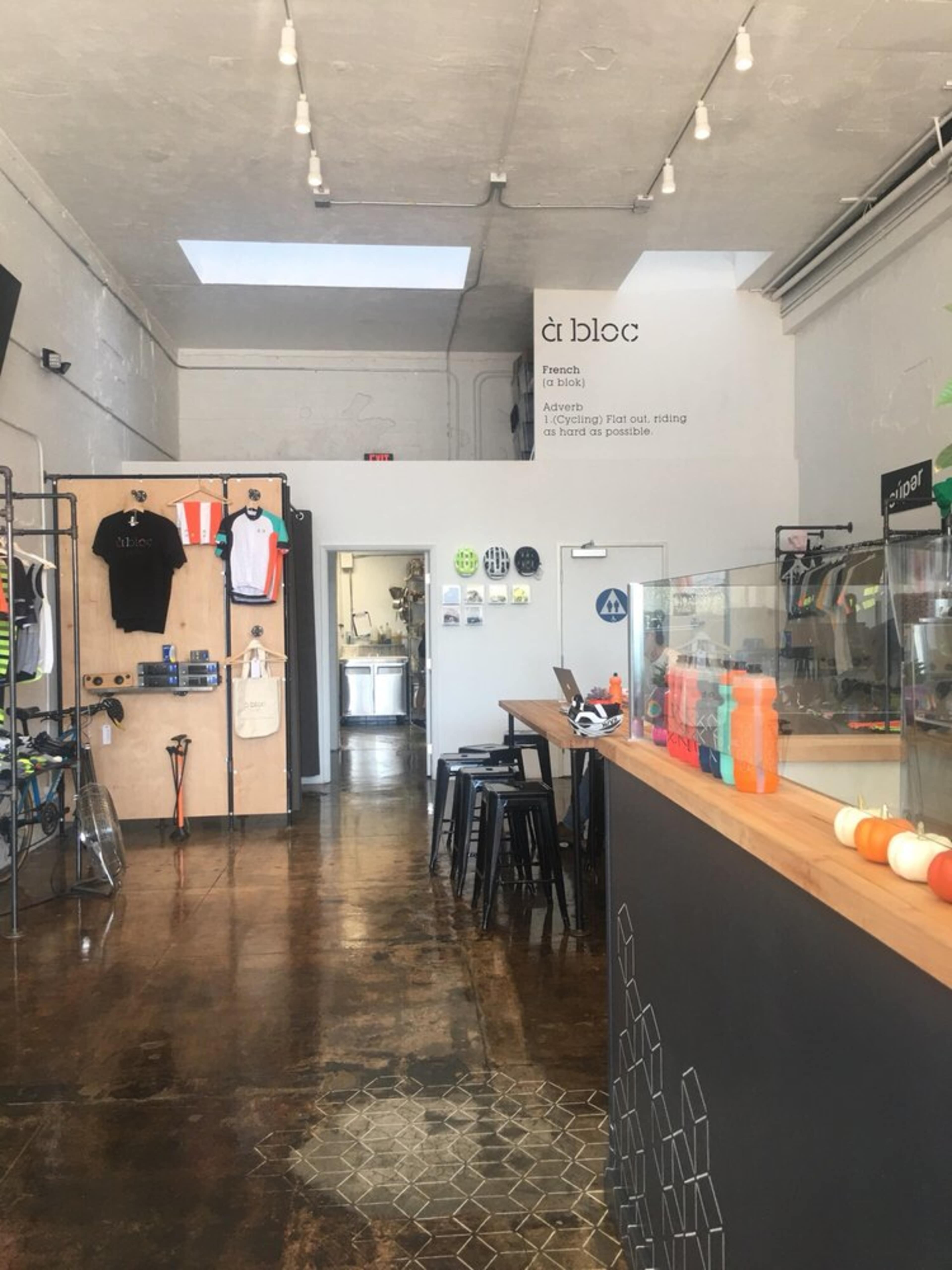 The interior of a modern bike shop features a long wooden counter, colorful cycling gear displayed on walls, and a clean, open space with soft lighting.