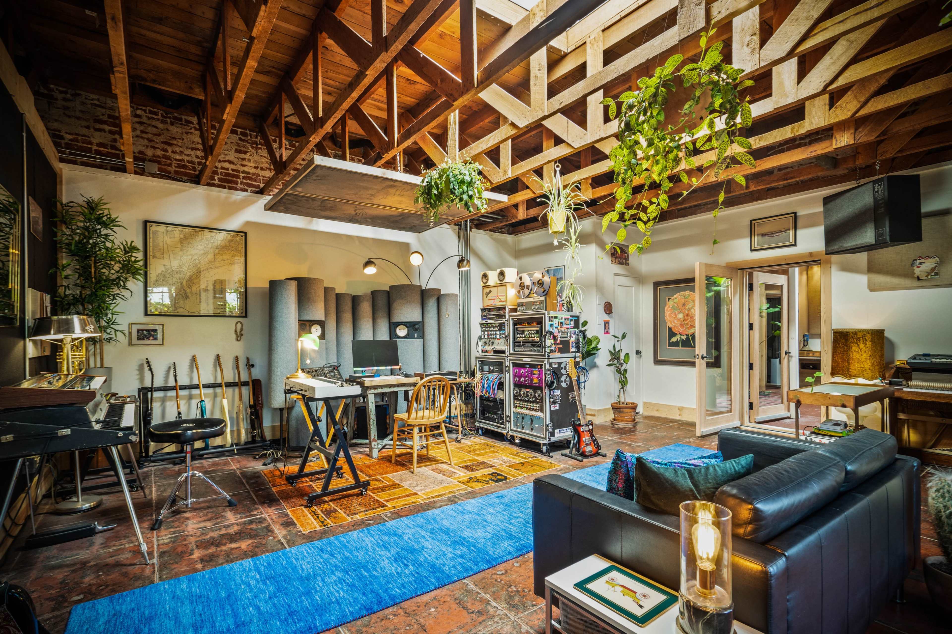 A spacious music studio with high wooden ceilings, various musical instruments, and vibrant plants arranged around a central seating area and workspace.
