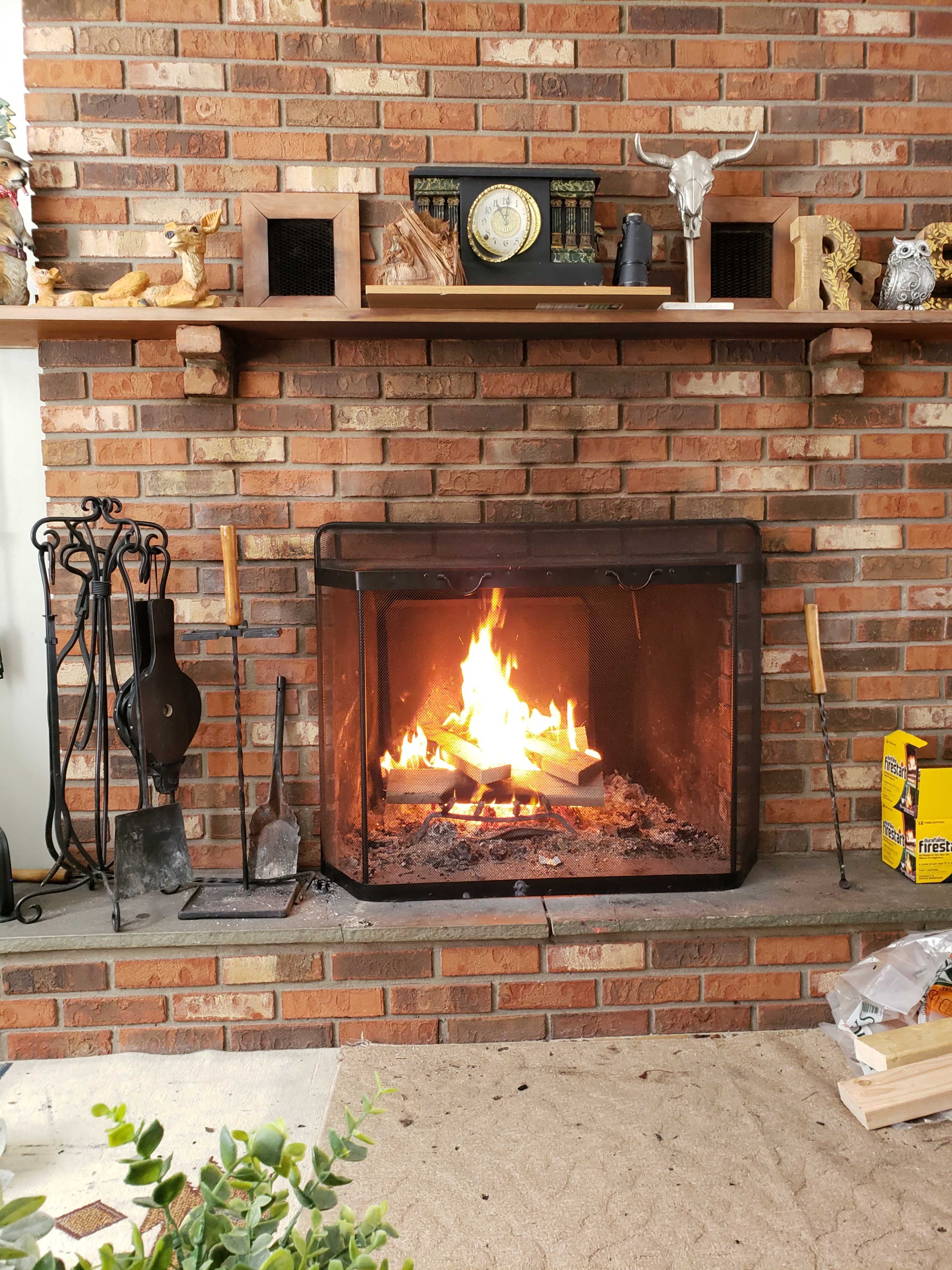 A fire burns in a brick fireplace surrounded by decorative items and tools for tending the fire.