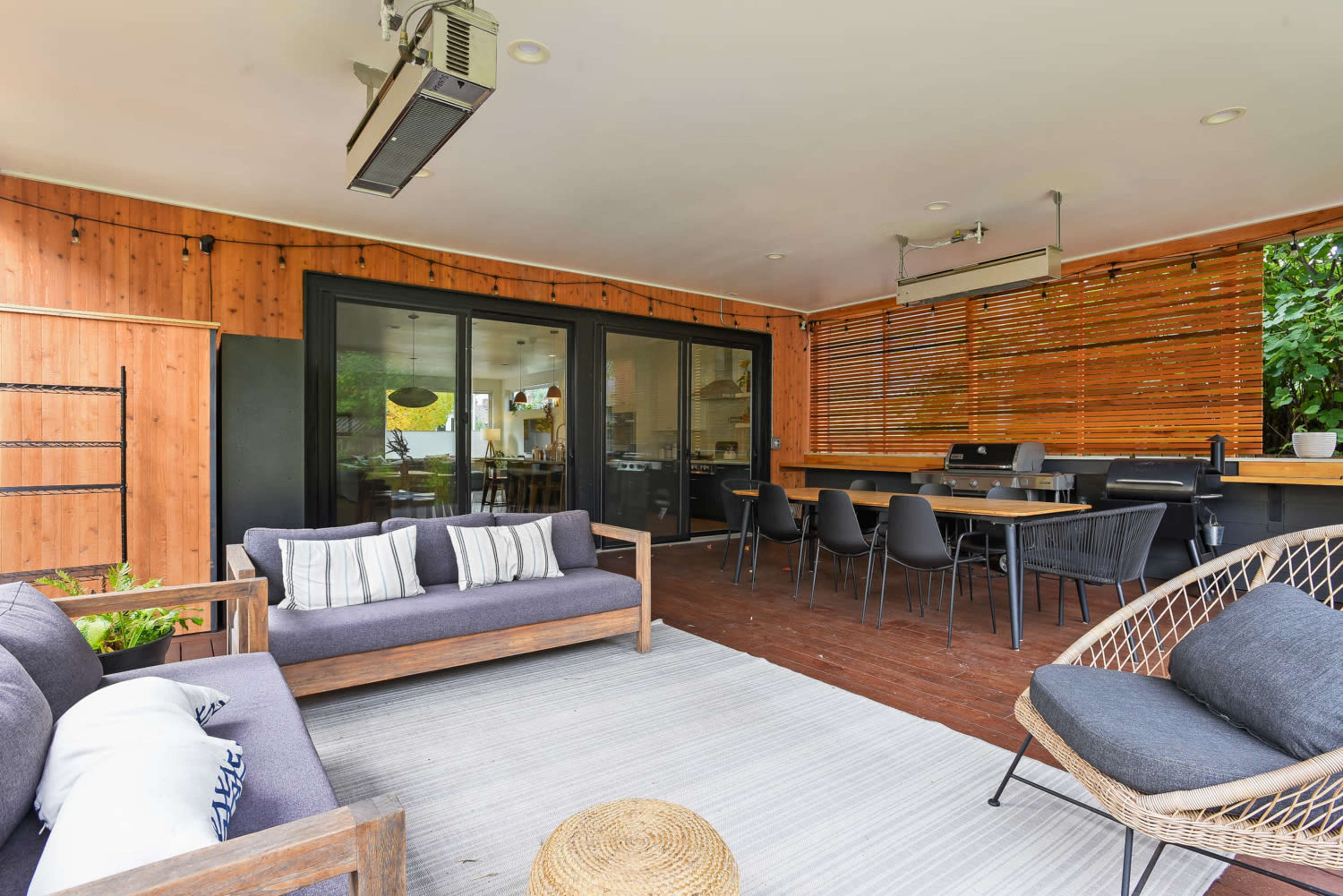 A covered outdoor seating area featuring modern furniture, a dining table, and wooden paneling.