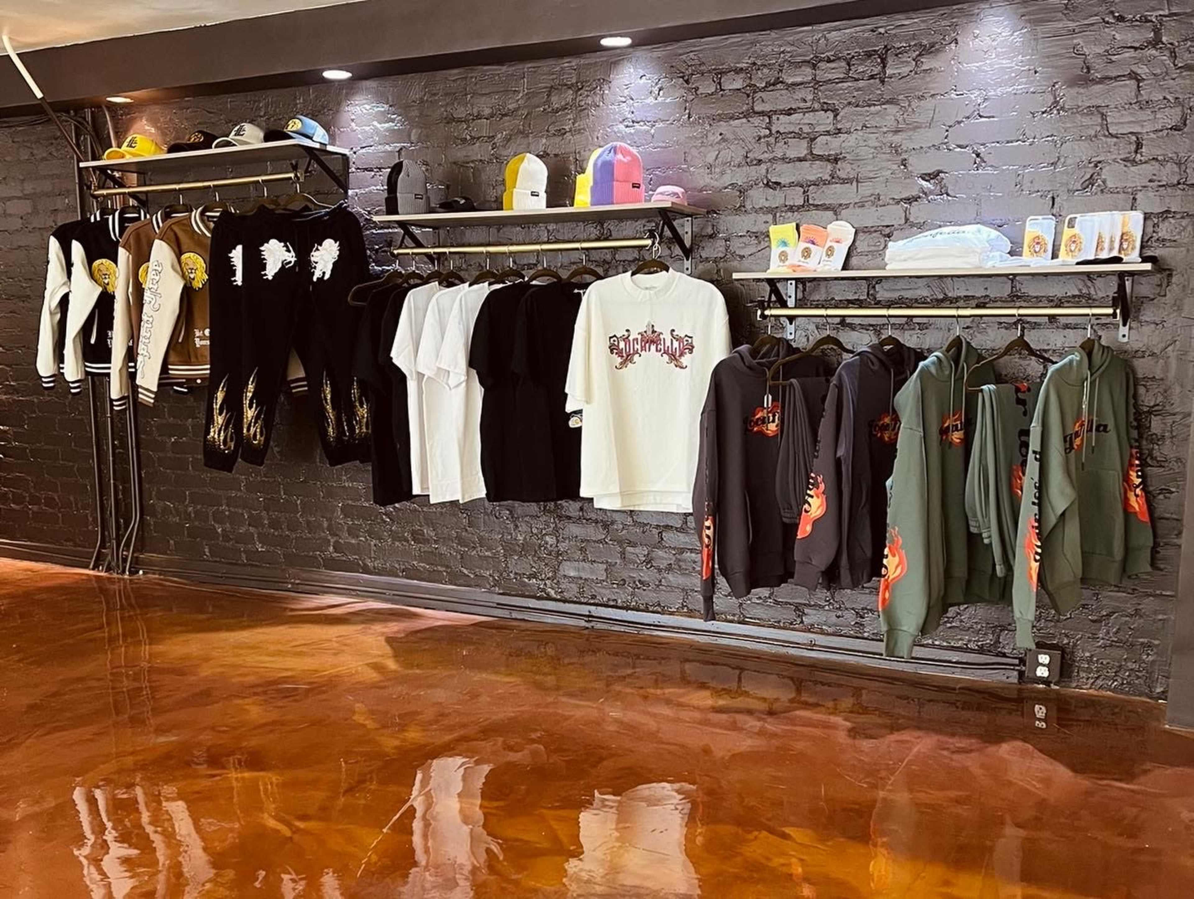 A clothing display featuring various sweatshirts, t-shirts, and hats arranged on hanging racks against a brick wall.
