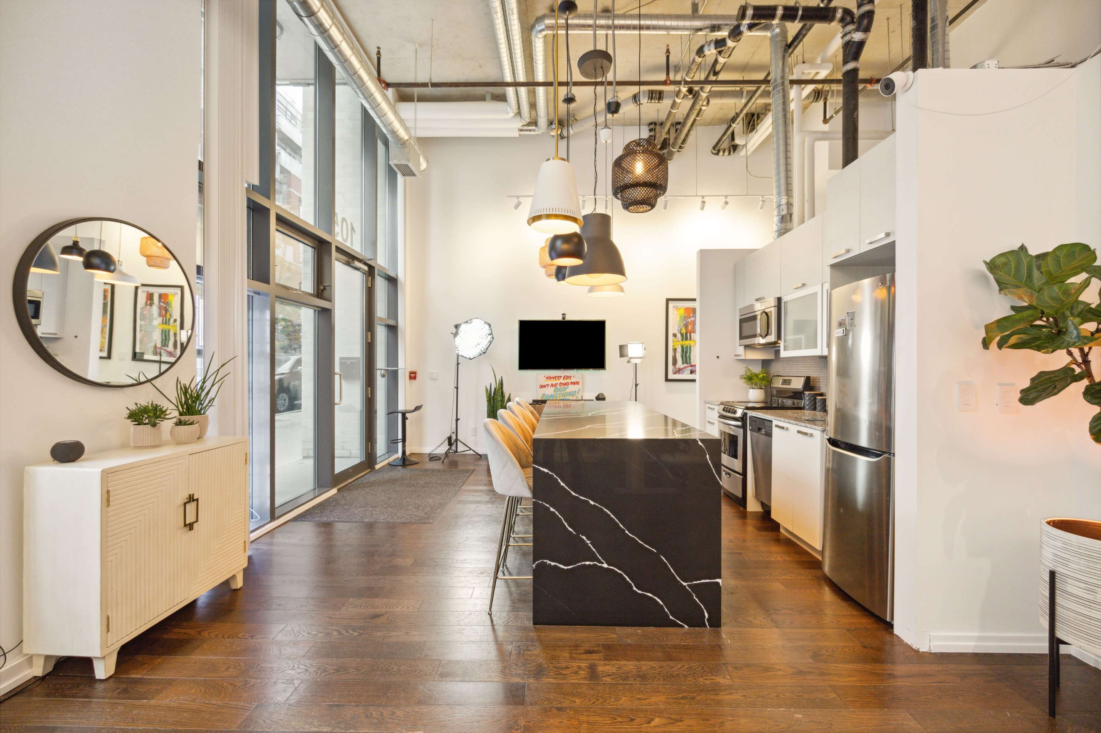 The image shows a modern kitchen with a large island featuring a black countertop, stainless steel appliances, and a dining area with orange chairs.