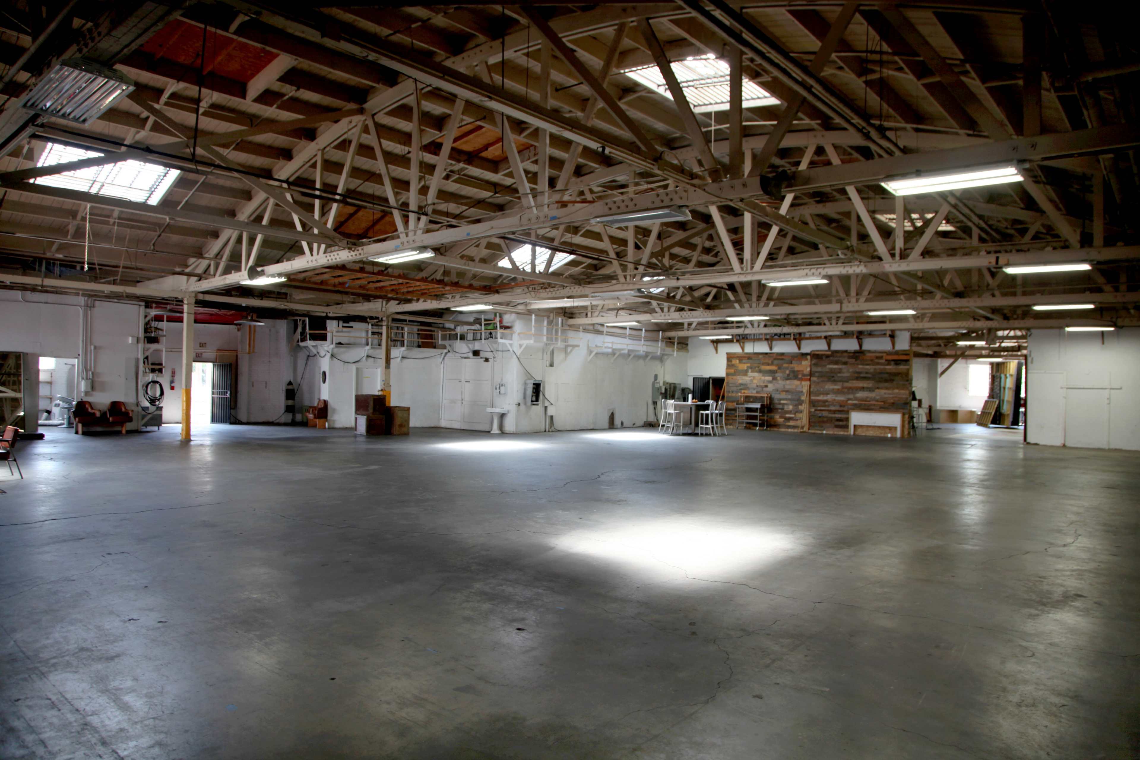 The image shows a spacious, empty industrial warehouse with exposed wooden beams and concrete flooring.