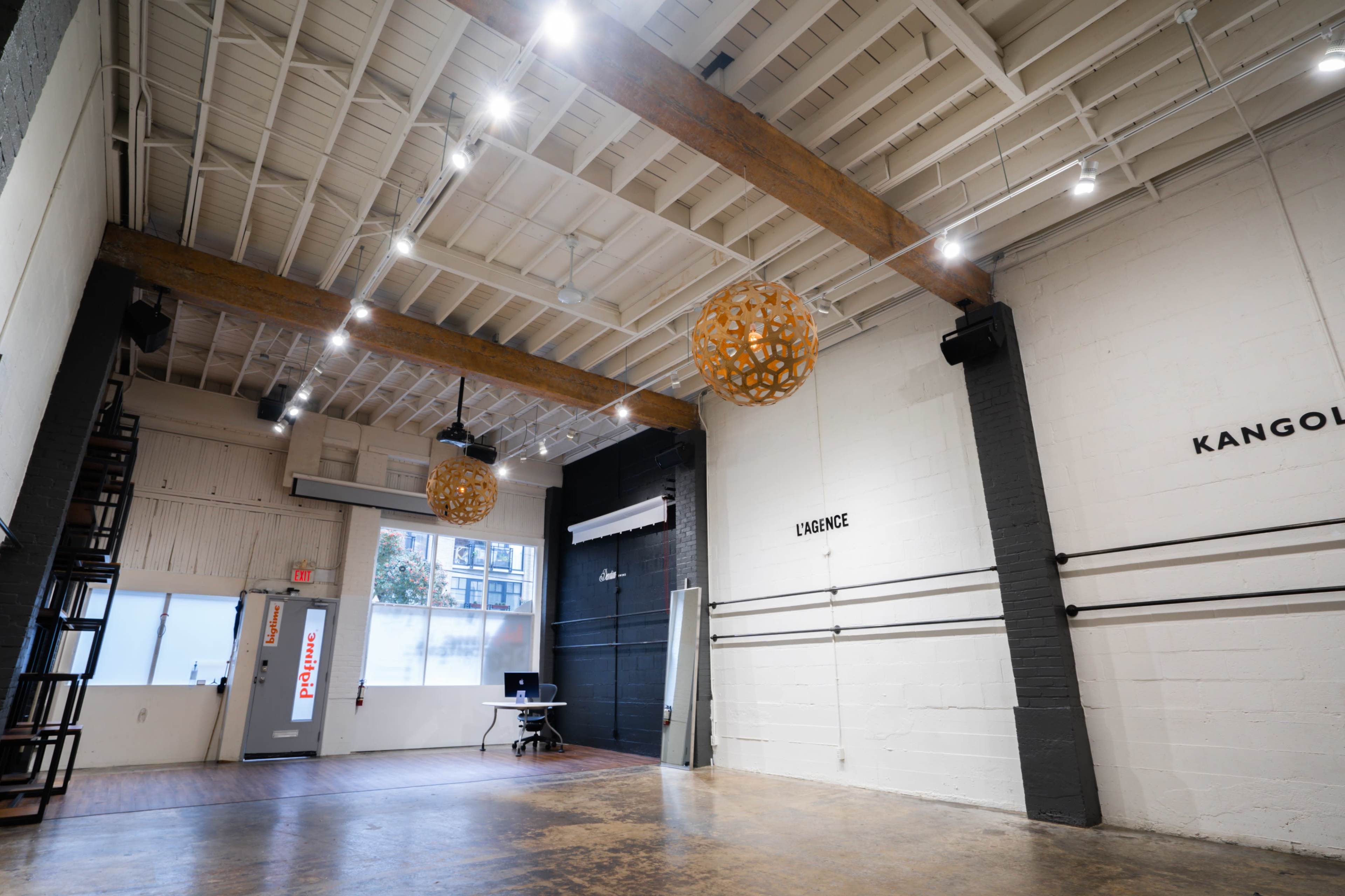 An open, well-lit space with wooden beams, two decorative light fixtures, and a black wall featuring the word "KANGOL" on one side.