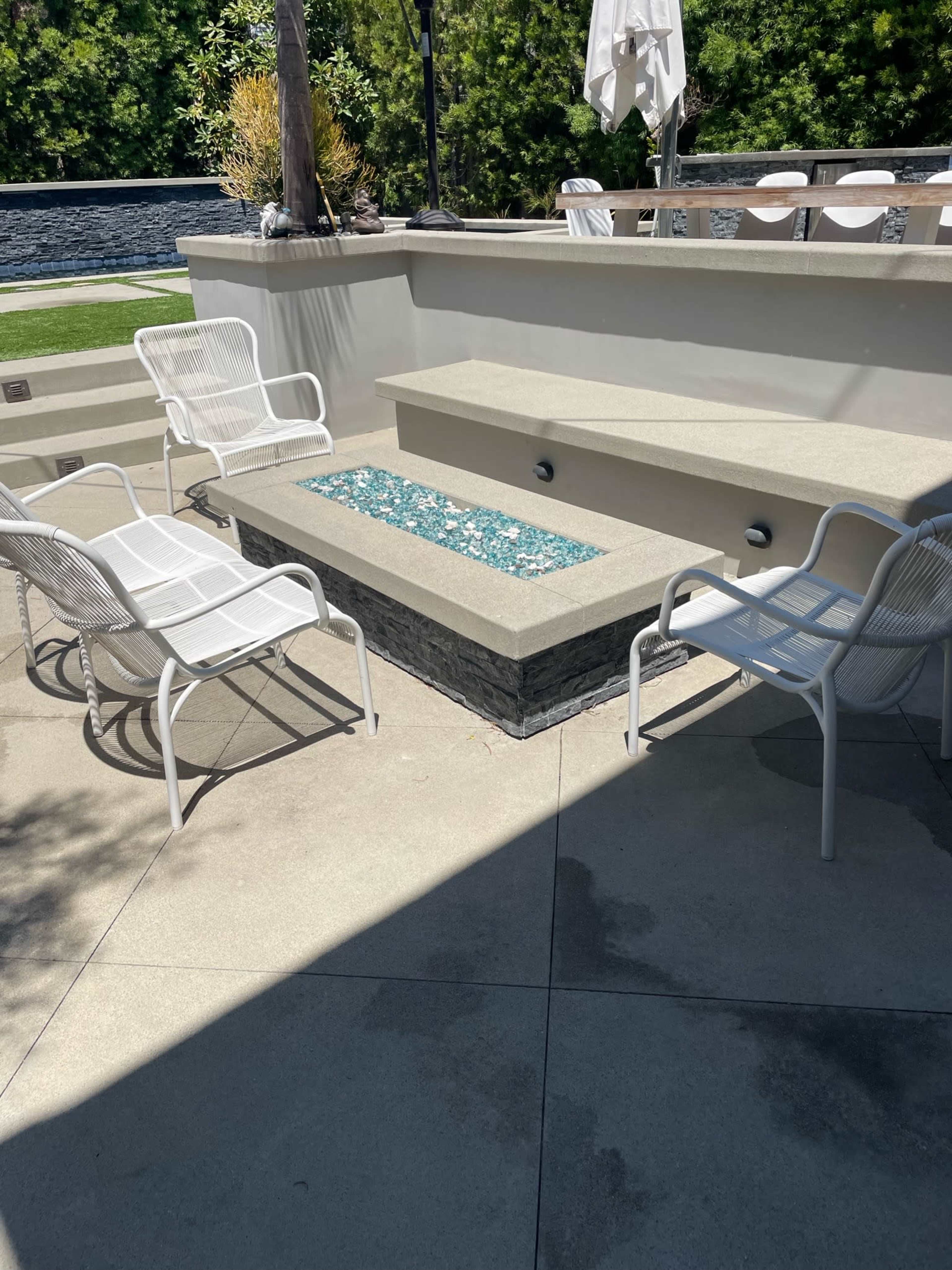 A sunlit outdoor seating area with white chairs arranged around a stone-accented platform featuring blue glass accents.