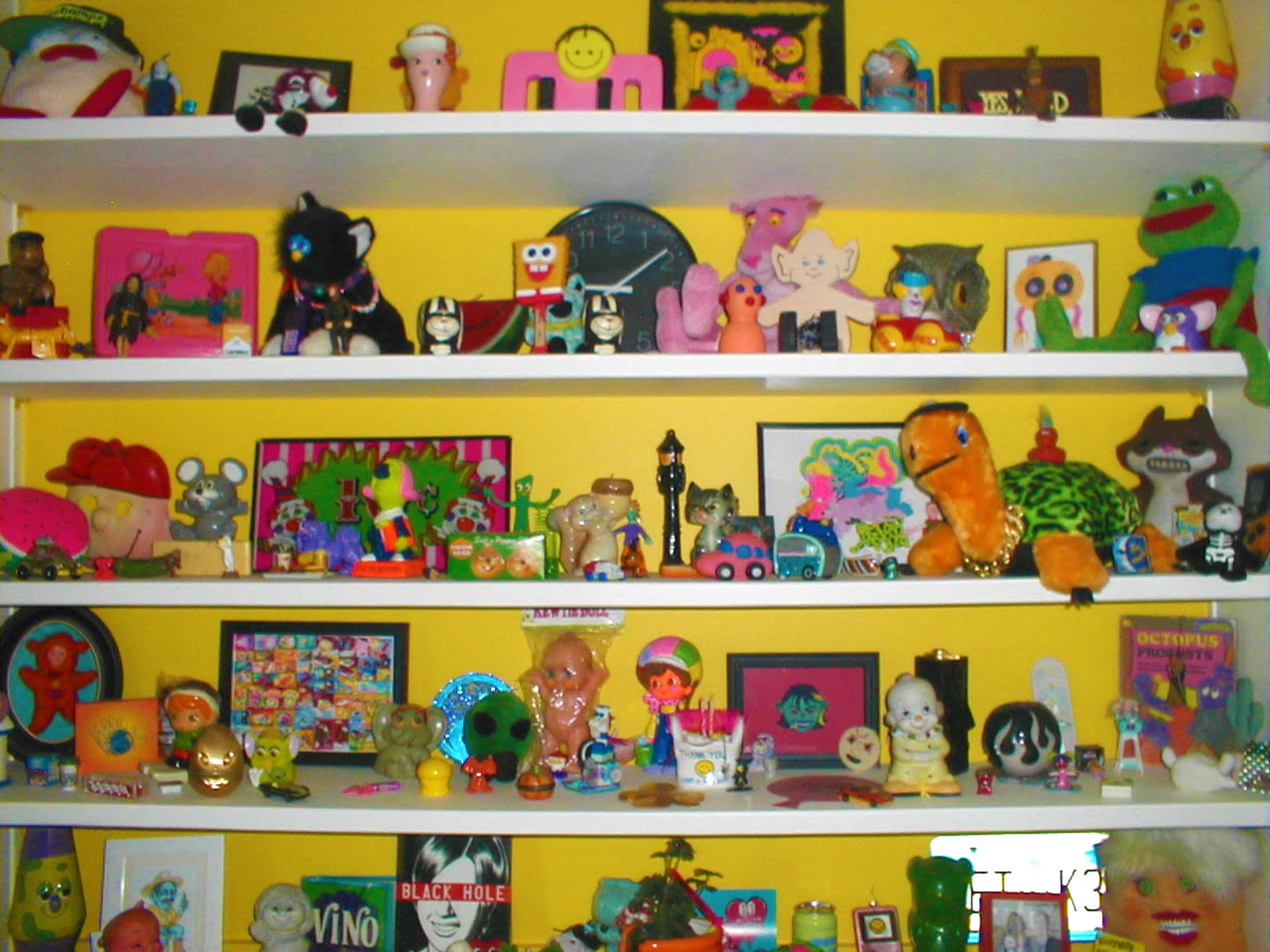 A brightly colored shelf displays a variety of toys, collectibles, and framed artworks arranged in a playful manner.
