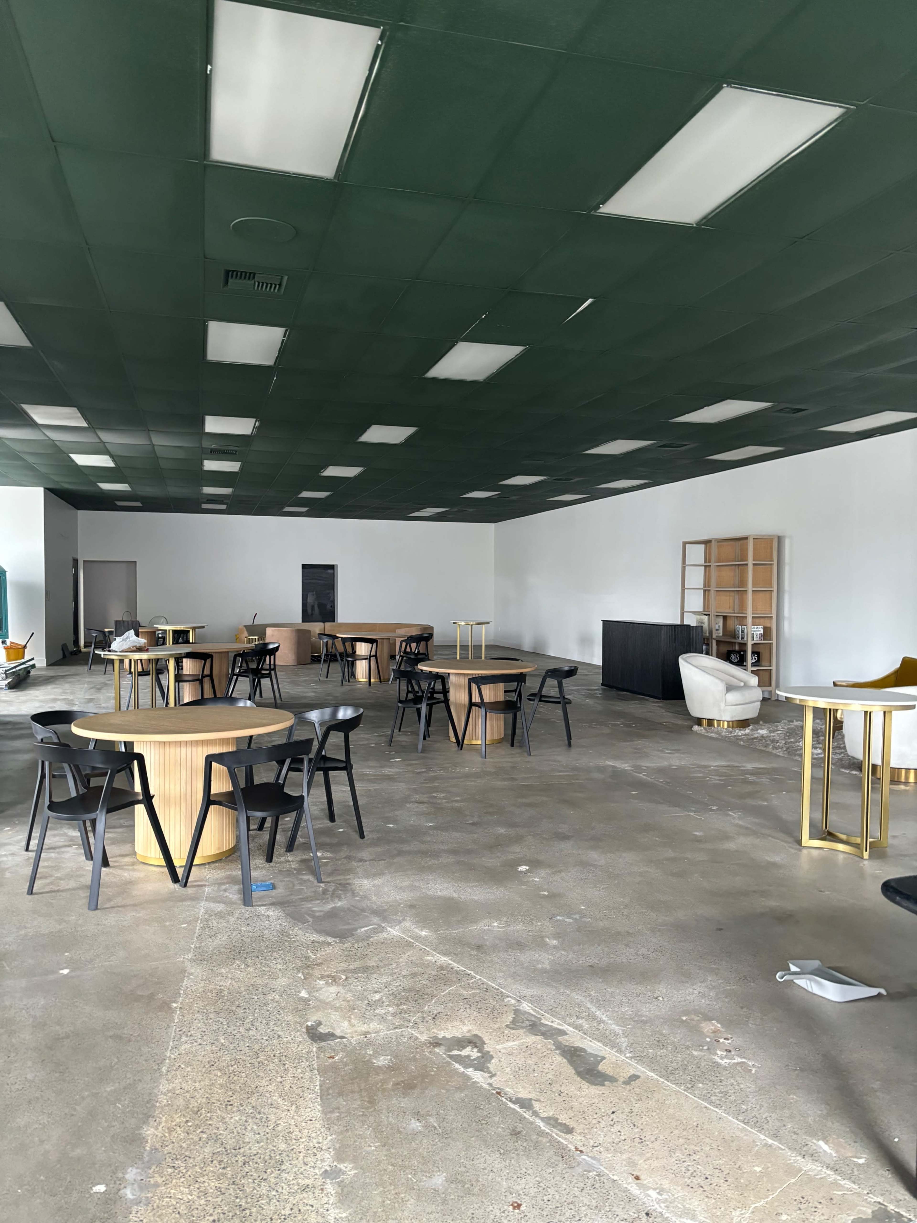 An empty room with several round tables, black chairs, and a few pieces of minimal furniture against the walls.