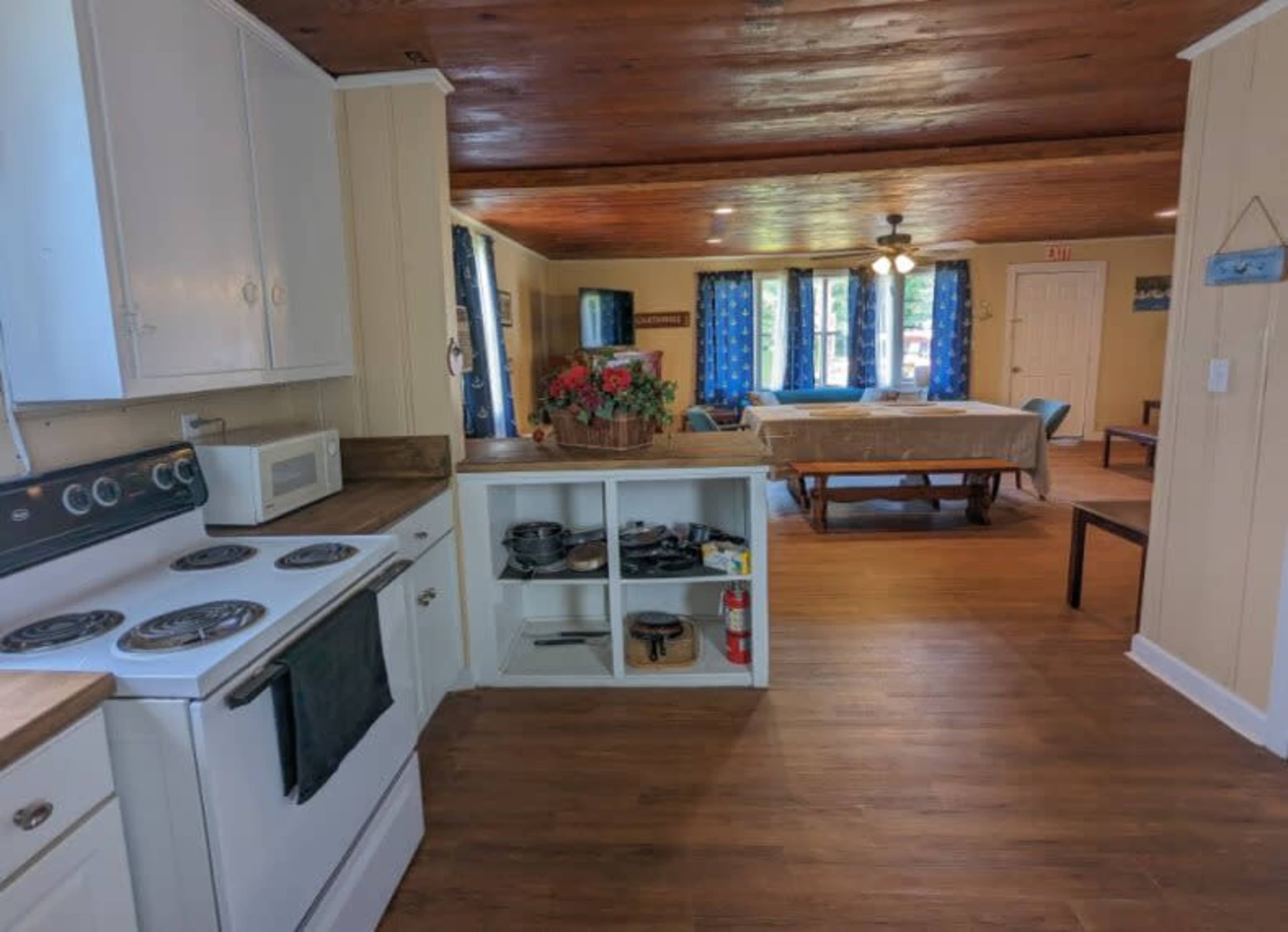 A kitchen area with a stove and microwave, leading into a living space with a table and seating.