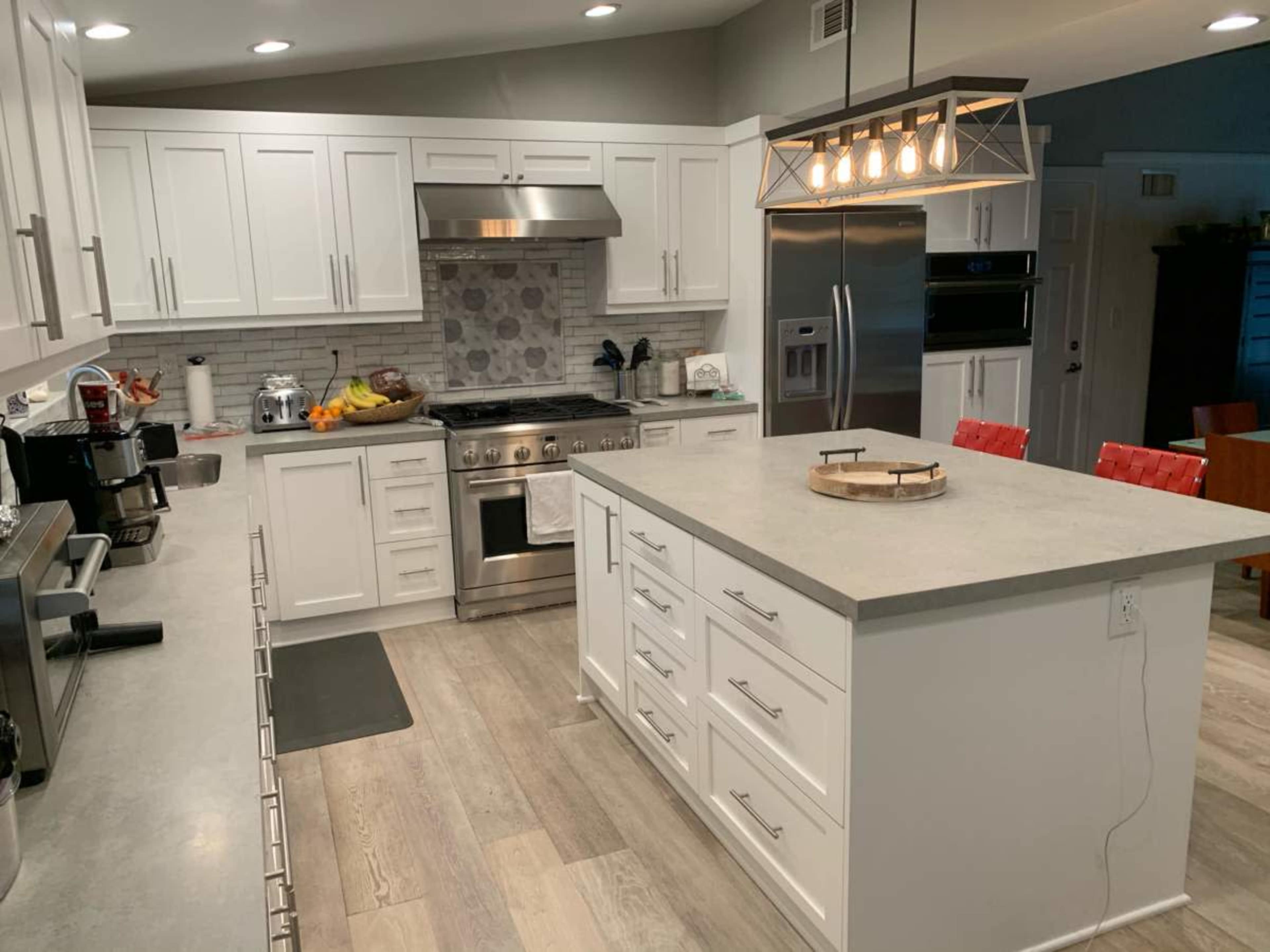 The image shows a modern kitchen with white cabinetry, a large island, stainless steel appliances, and a pendant light fixture.