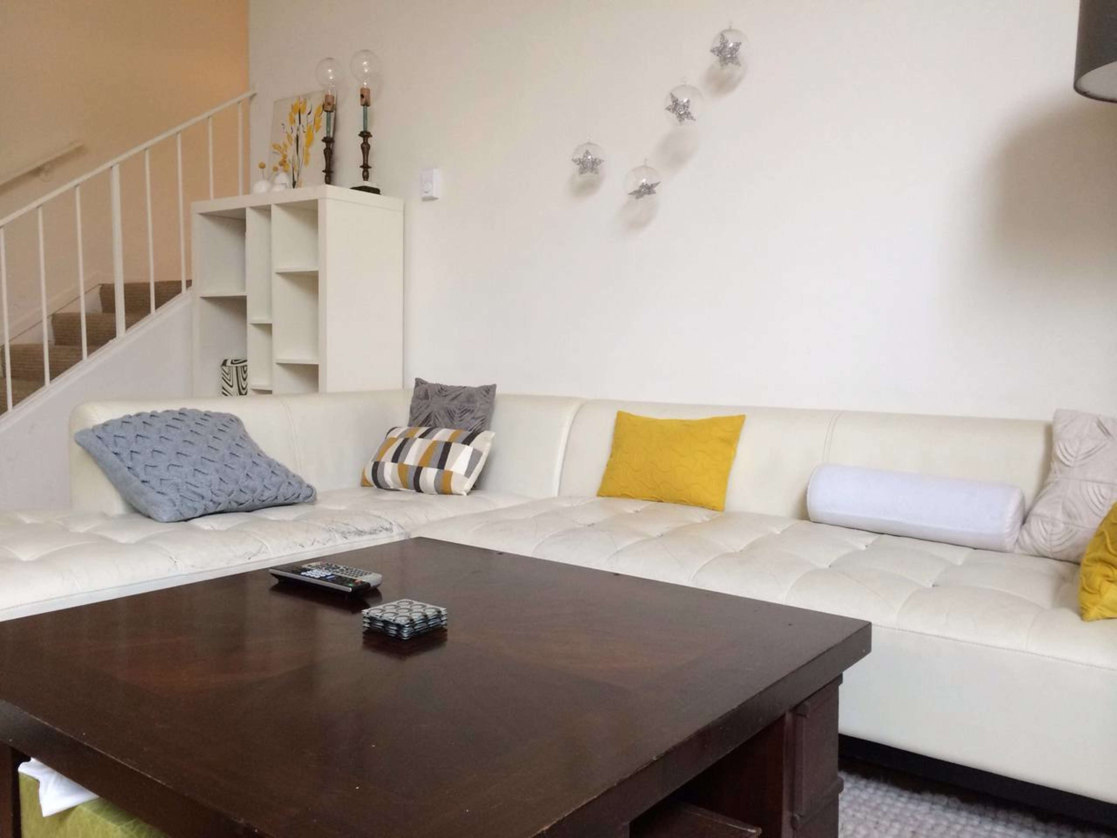 A modern living room featuring a white sectional sofa with decorative pillows, a wooden coffee table, and a staircase in the background.