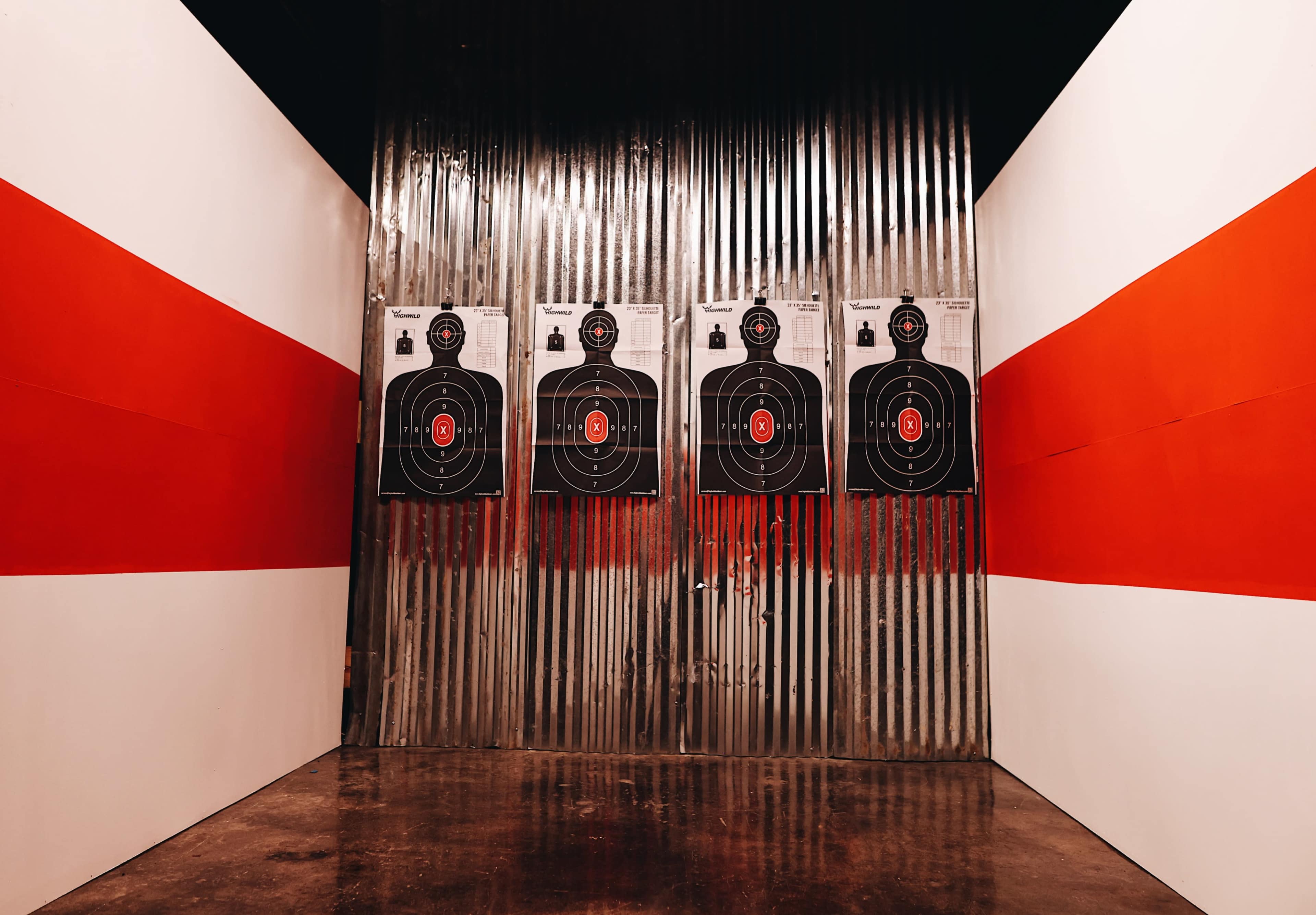 The image shows a shooting range with targets mounted on a metallic wall, flanked by red and white-painted walls.