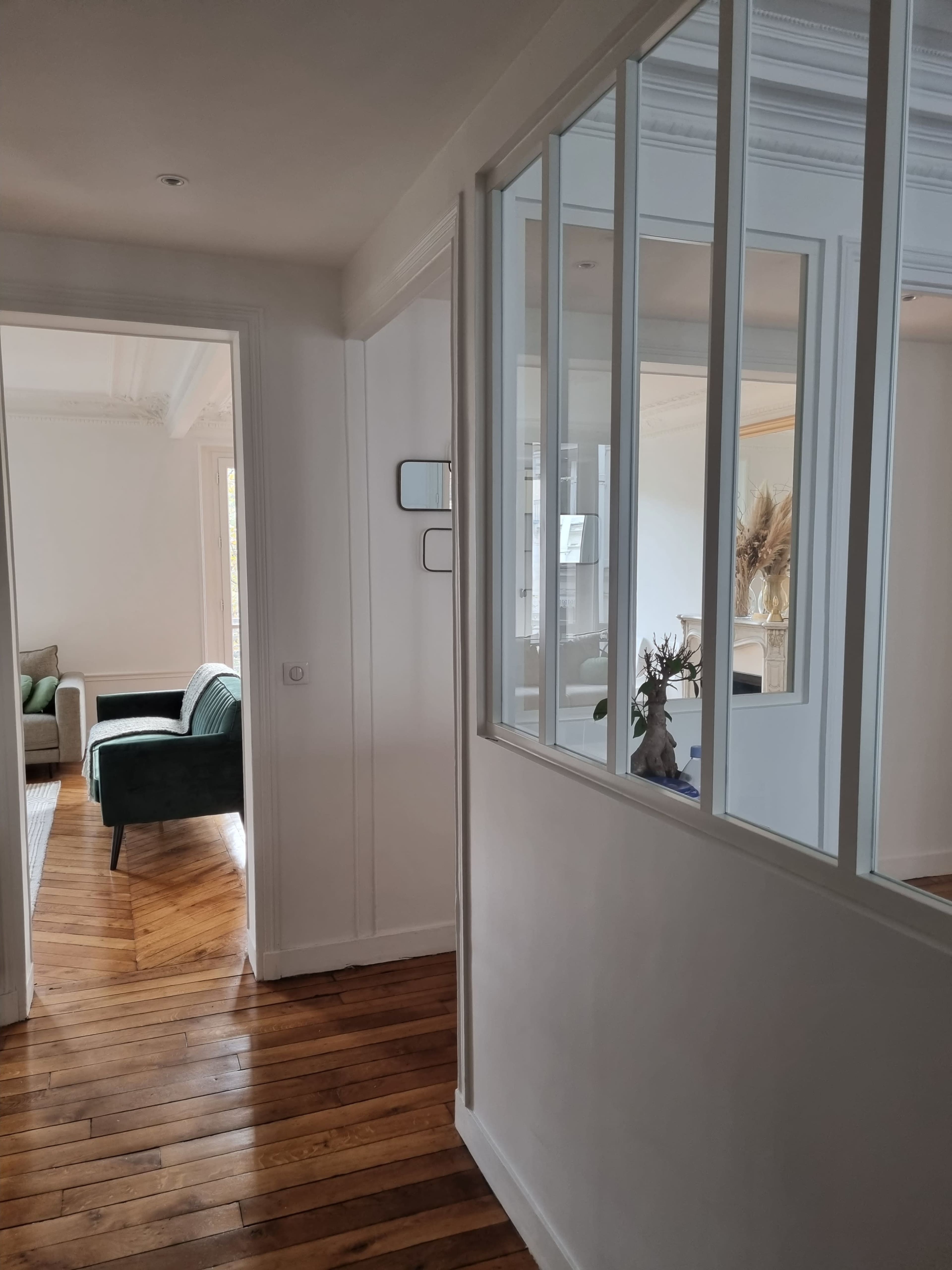 A hallway featuring wooden flooring and glass partition walls leads to a bright living area.