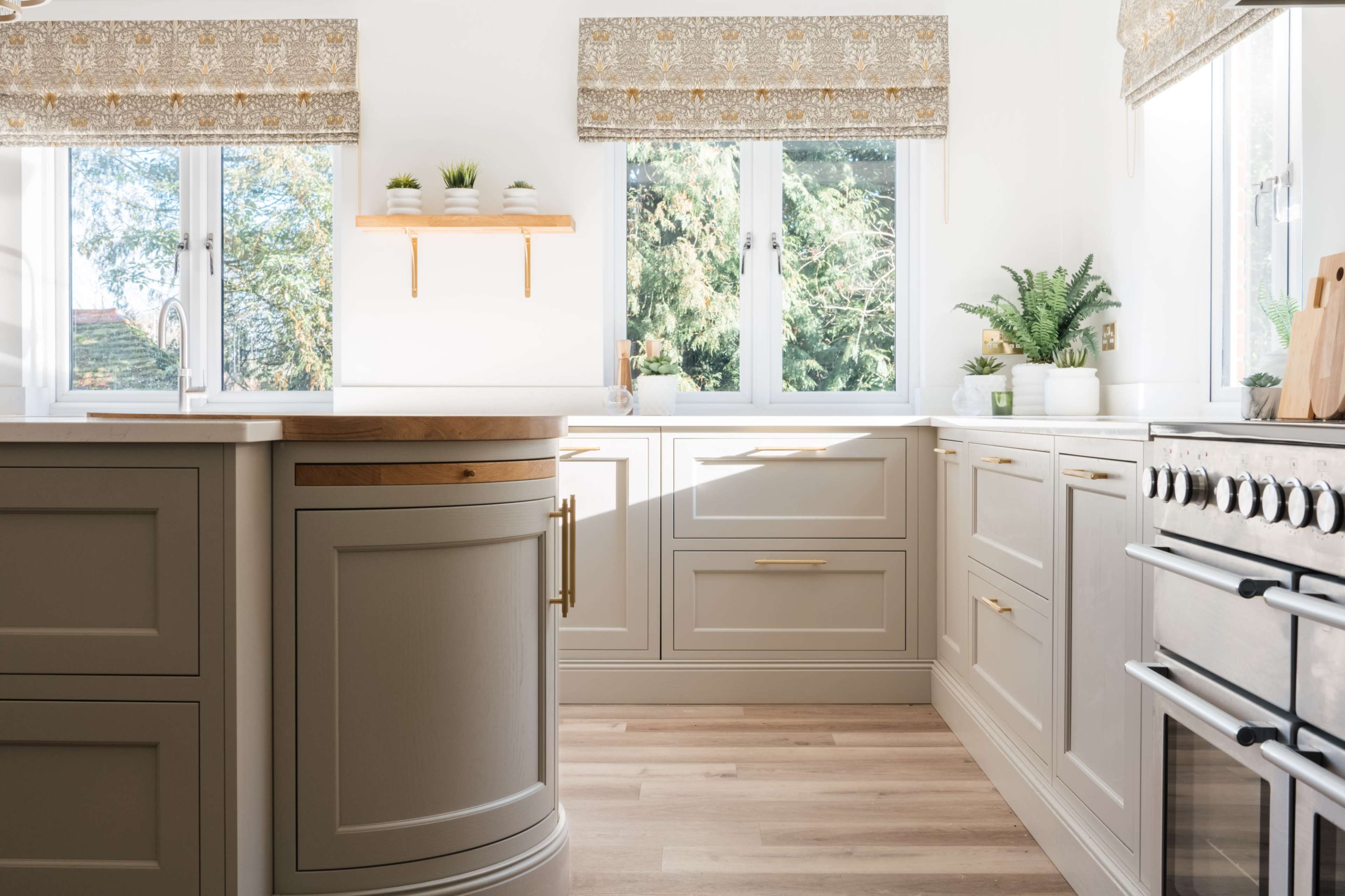 A well-lit kitchen features light-colored cabinetry, a wooden countertop, and plants arranged on shelves and windowsills.