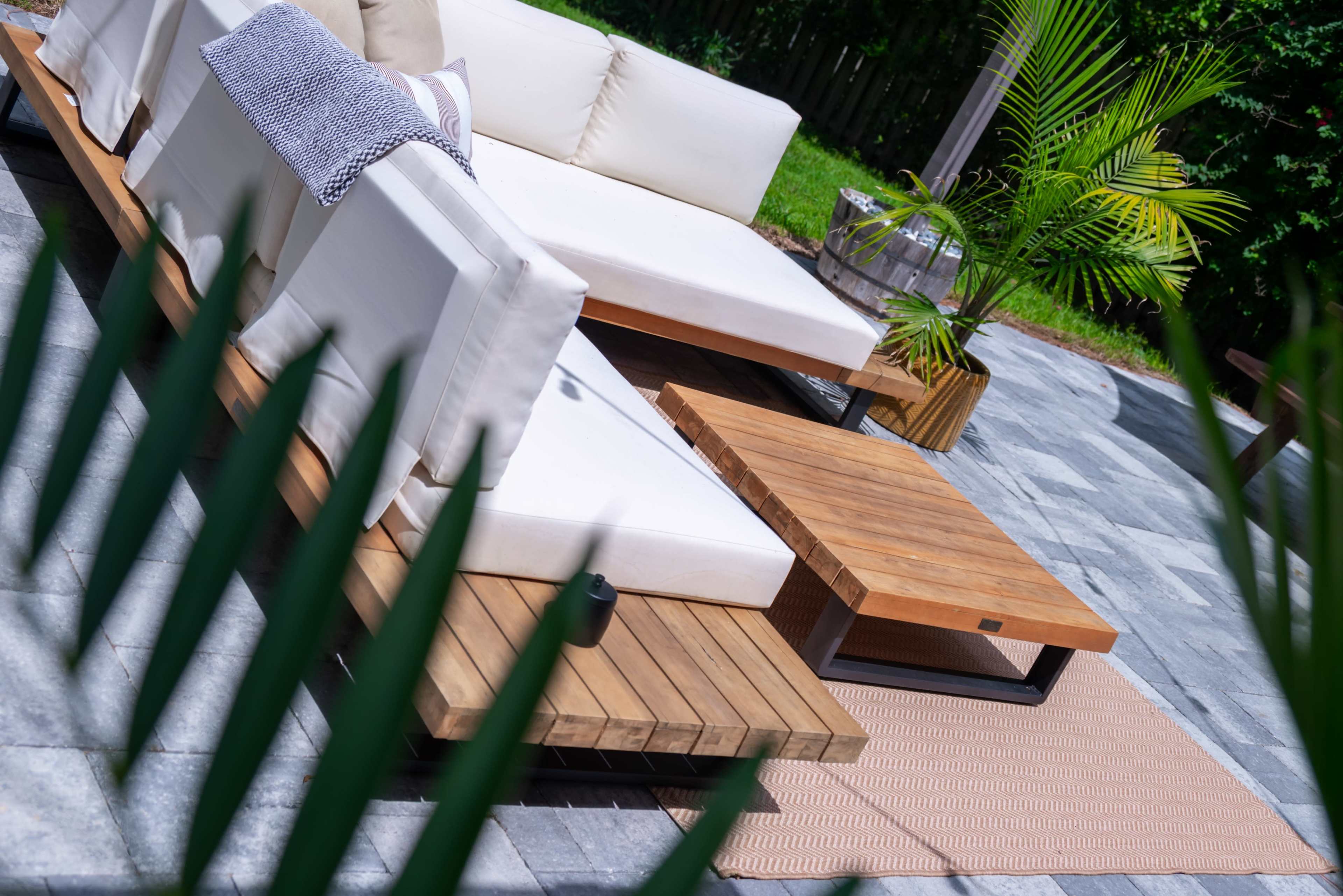 A modern outdoor seating area features white cushioned sofas, a wooden coffee table, and a decorative plant on a stone patio.