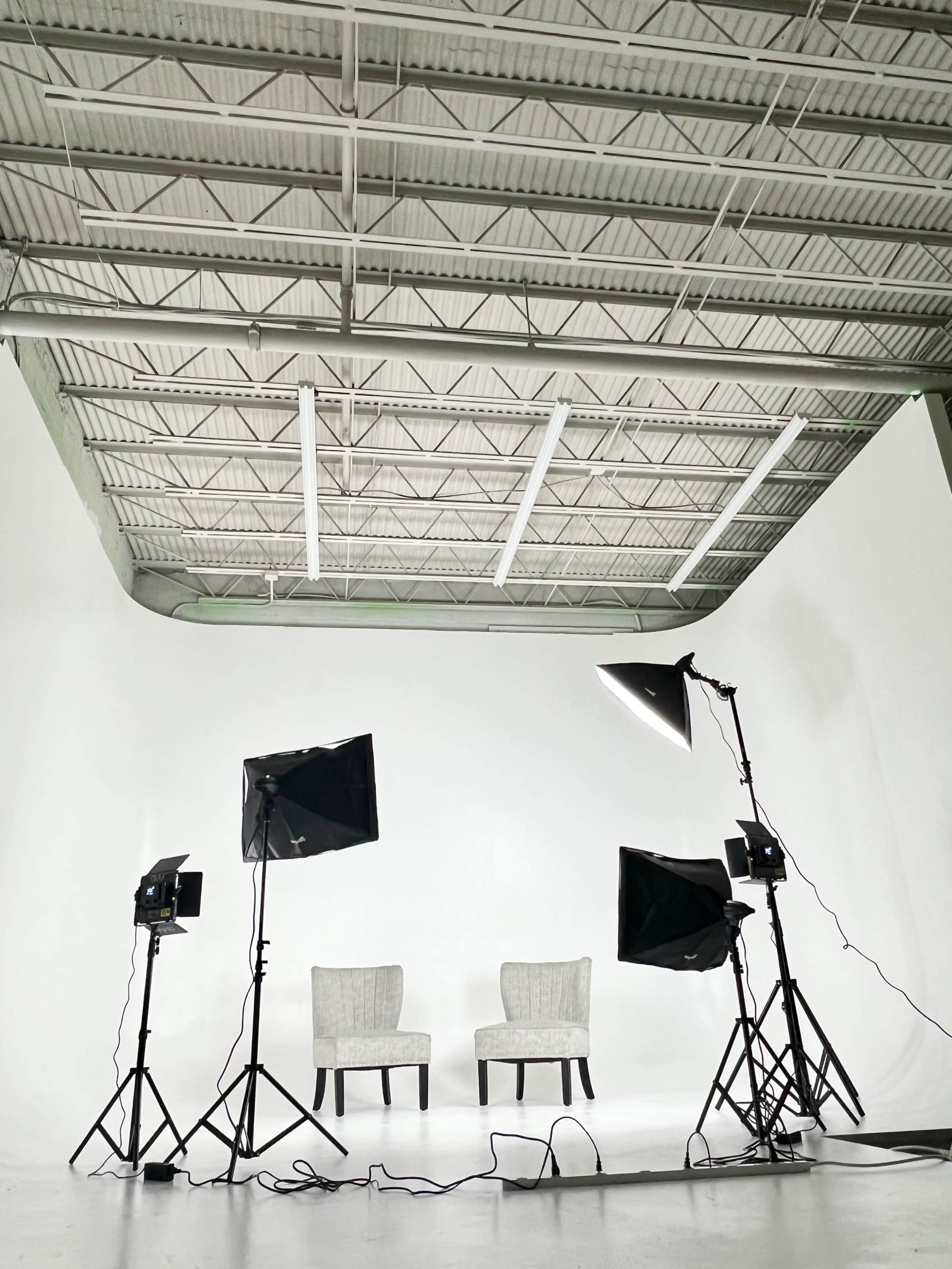 A minimalist studio setup with two chairs positioned in front of bright lighting equipment against a white backdrop.