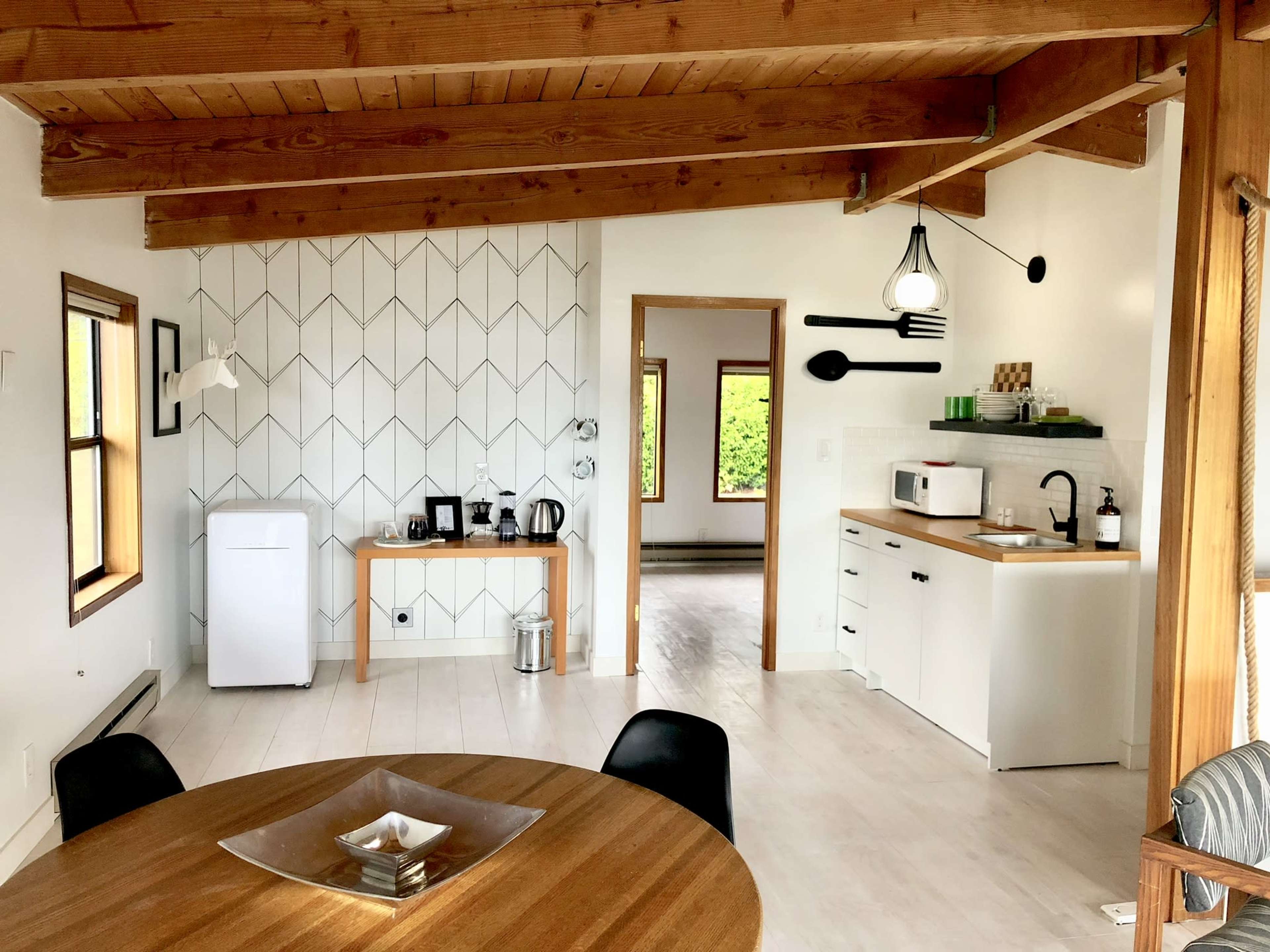 A modern, open-concept kitchen and dining area with wooden beams, a round dining table, and white cabinetry.