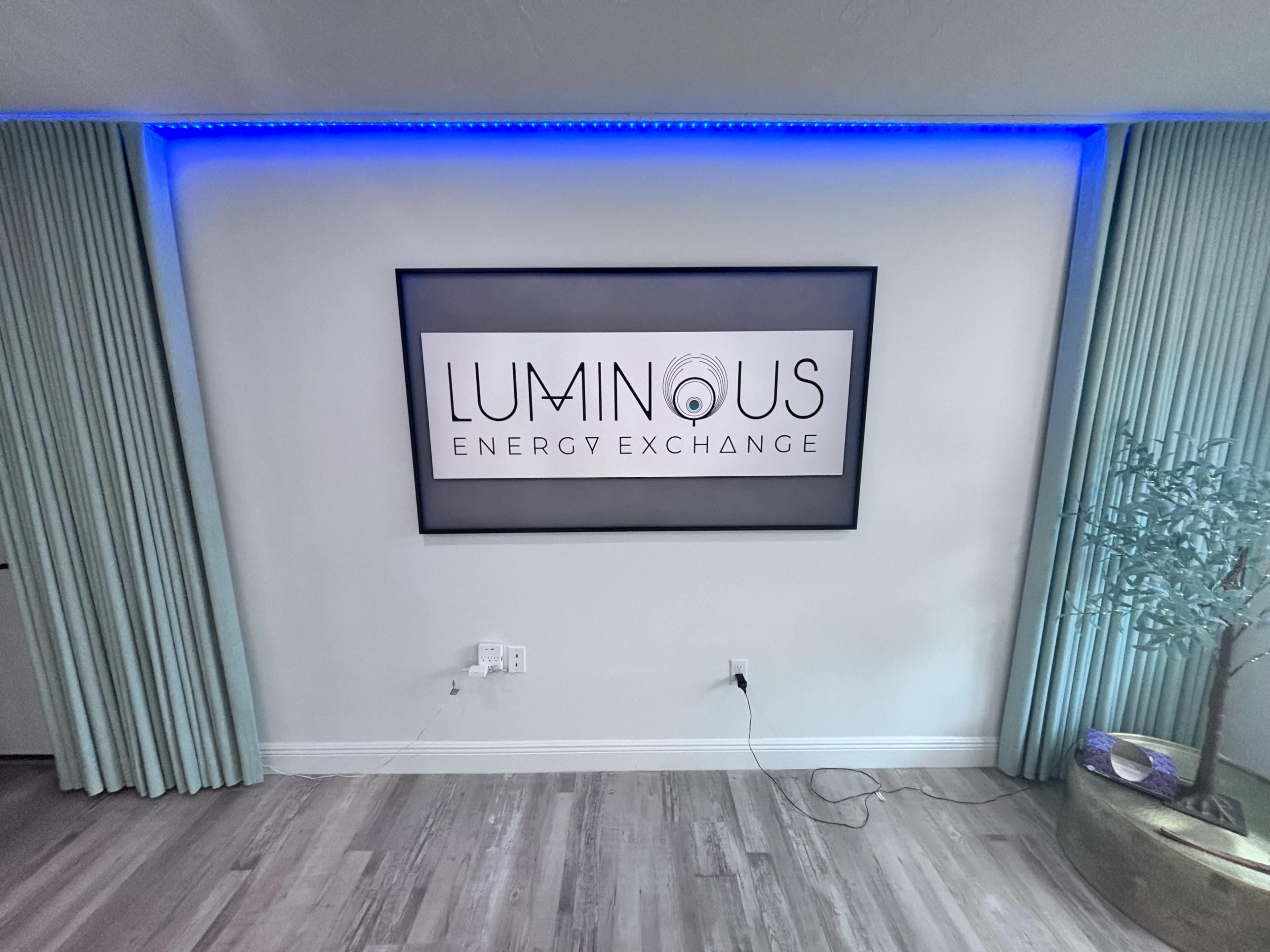 A wall features a framed display with the words "LUMINOUS ENERGY EXCHANGE" illuminated by blue lighting, flanked by light green curtains.