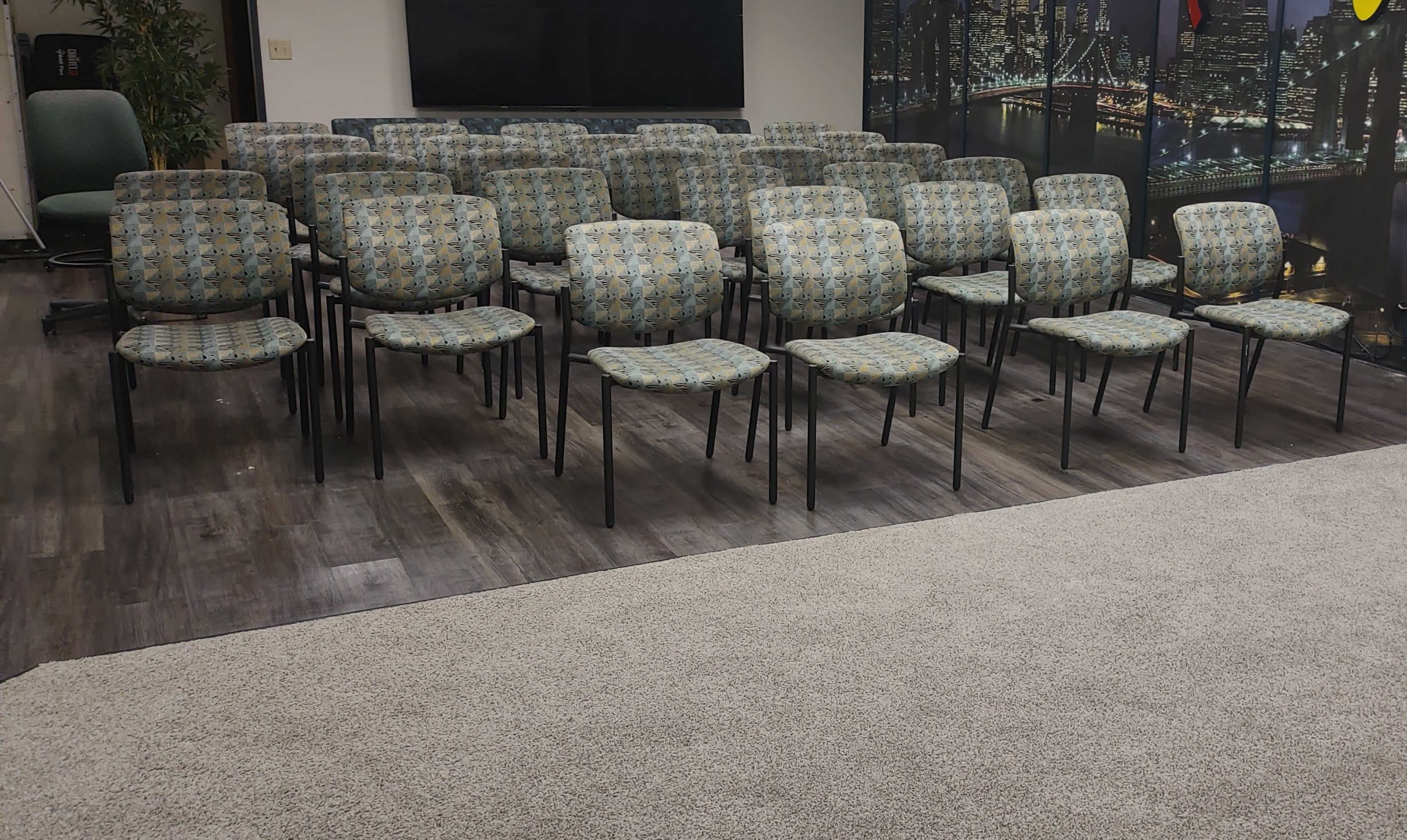A room filled with rows of upholstered chairs facing a blank wall with a large screen.
