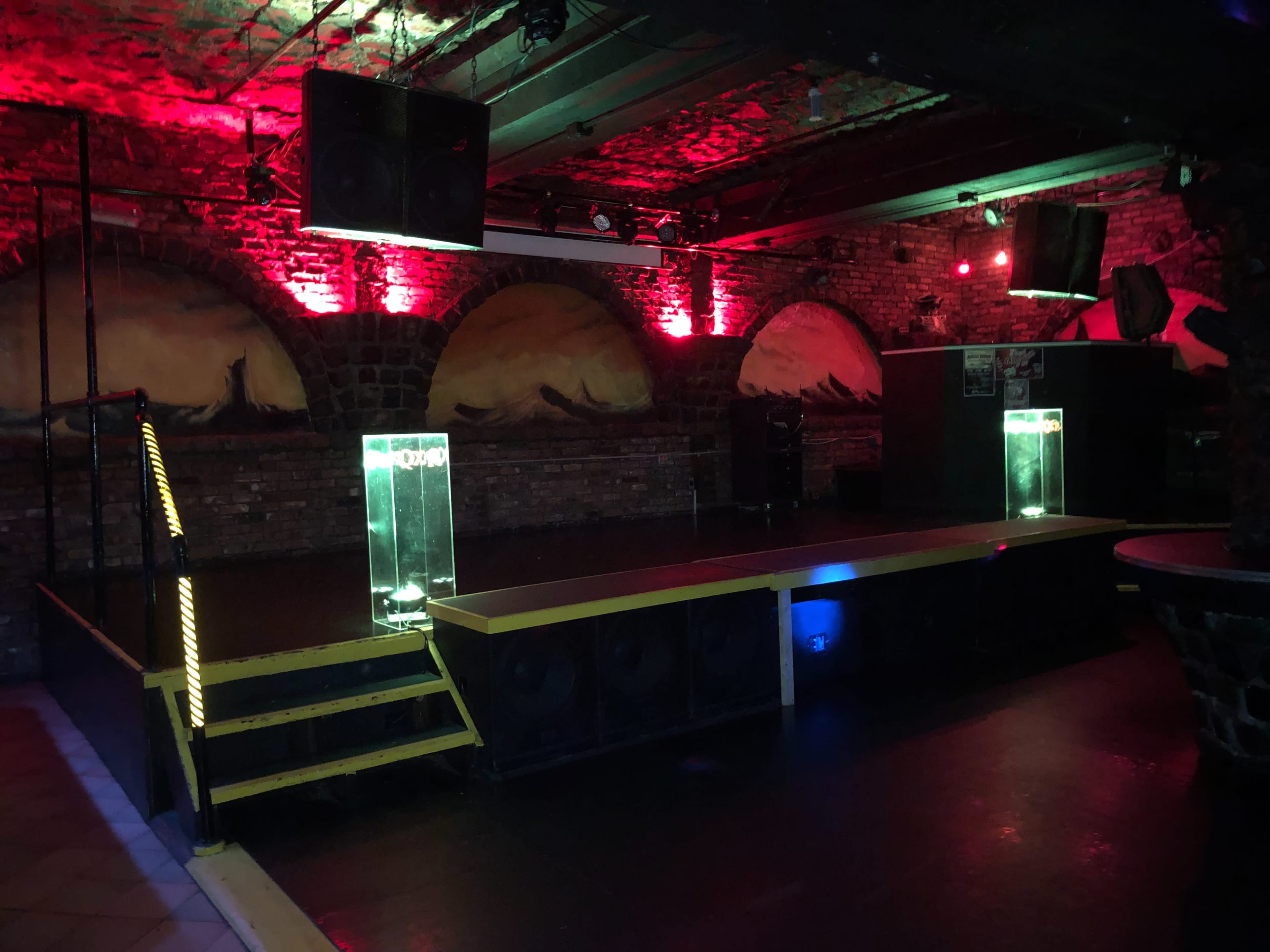 An empty stage in a dimly lit nightclub with red lighting and brick walls.