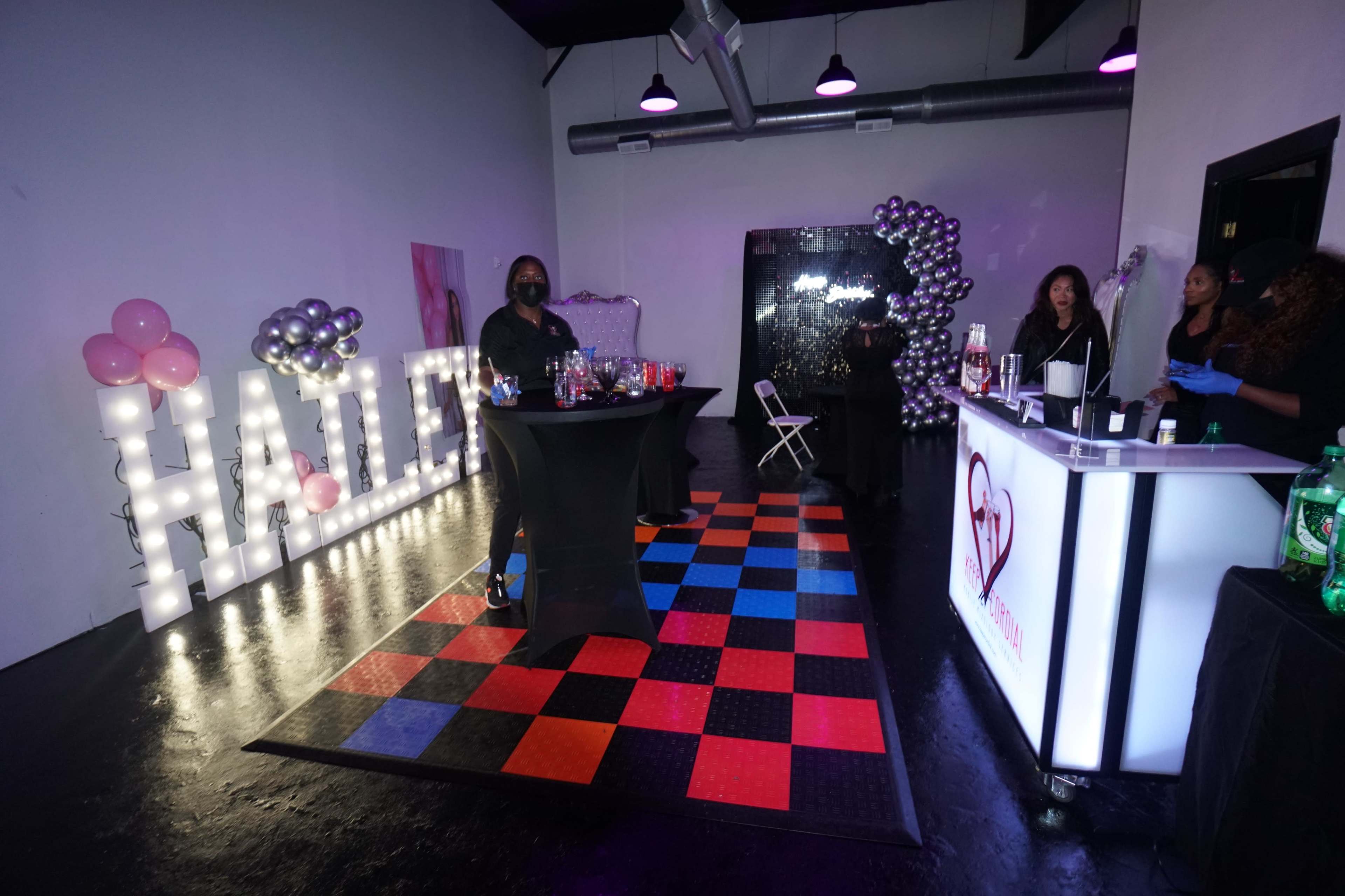 A vibrant event space featuring a drinks table, decorative balloons, and illuminated letters spelling "HALF."