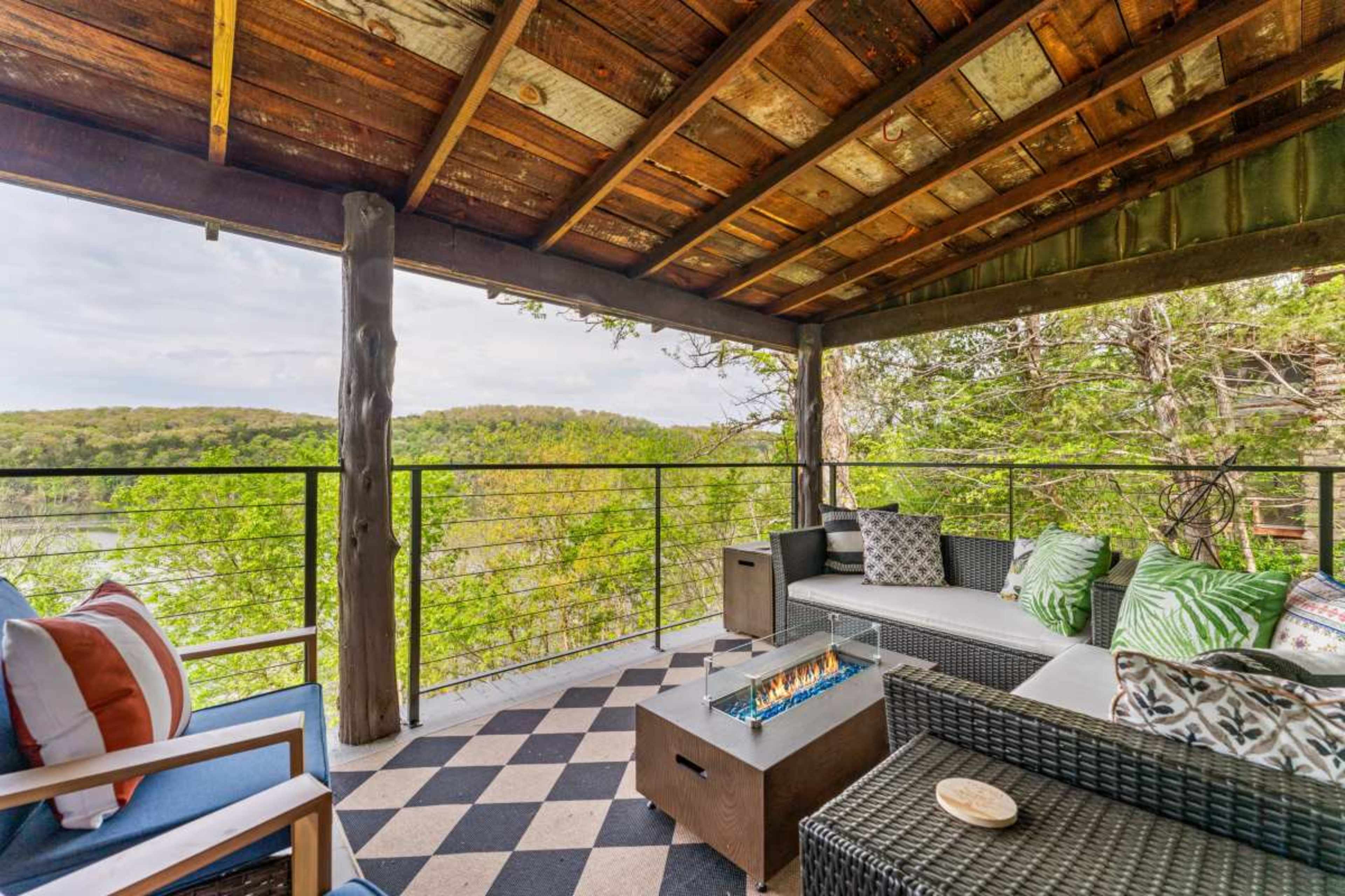 A spacious outdoor seating area features a fire pit, surrounded by comfortable furniture and a view of lush greenery.