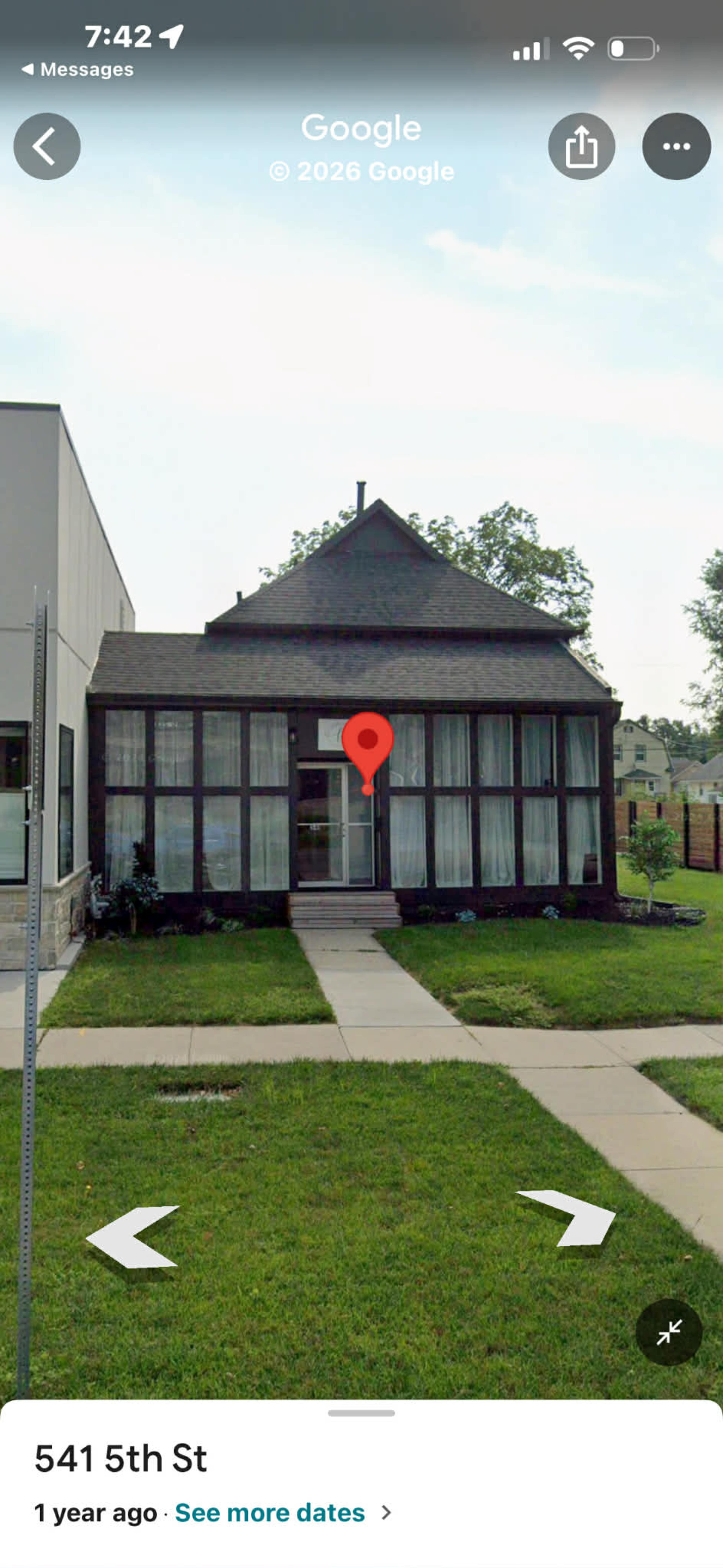 The image shows a house with a dark wooden façade, a peaked roof, and a front porch surrounded by a well-maintained lawn and sidewalk.