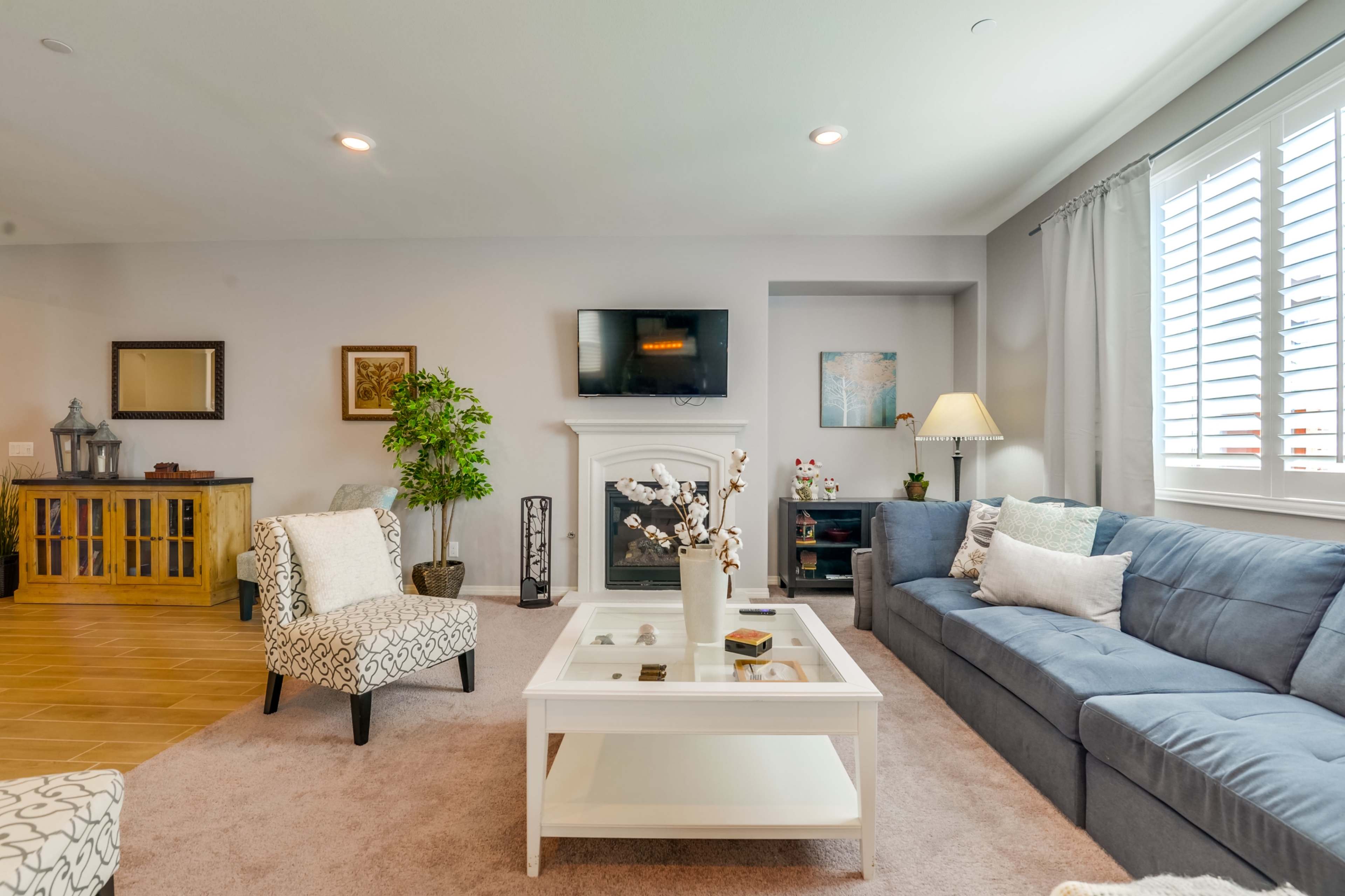 A modern living room featuring a blue sofa, an armchair with a patterned fabric, a coffee table, and a TV mounted above a fireplace.