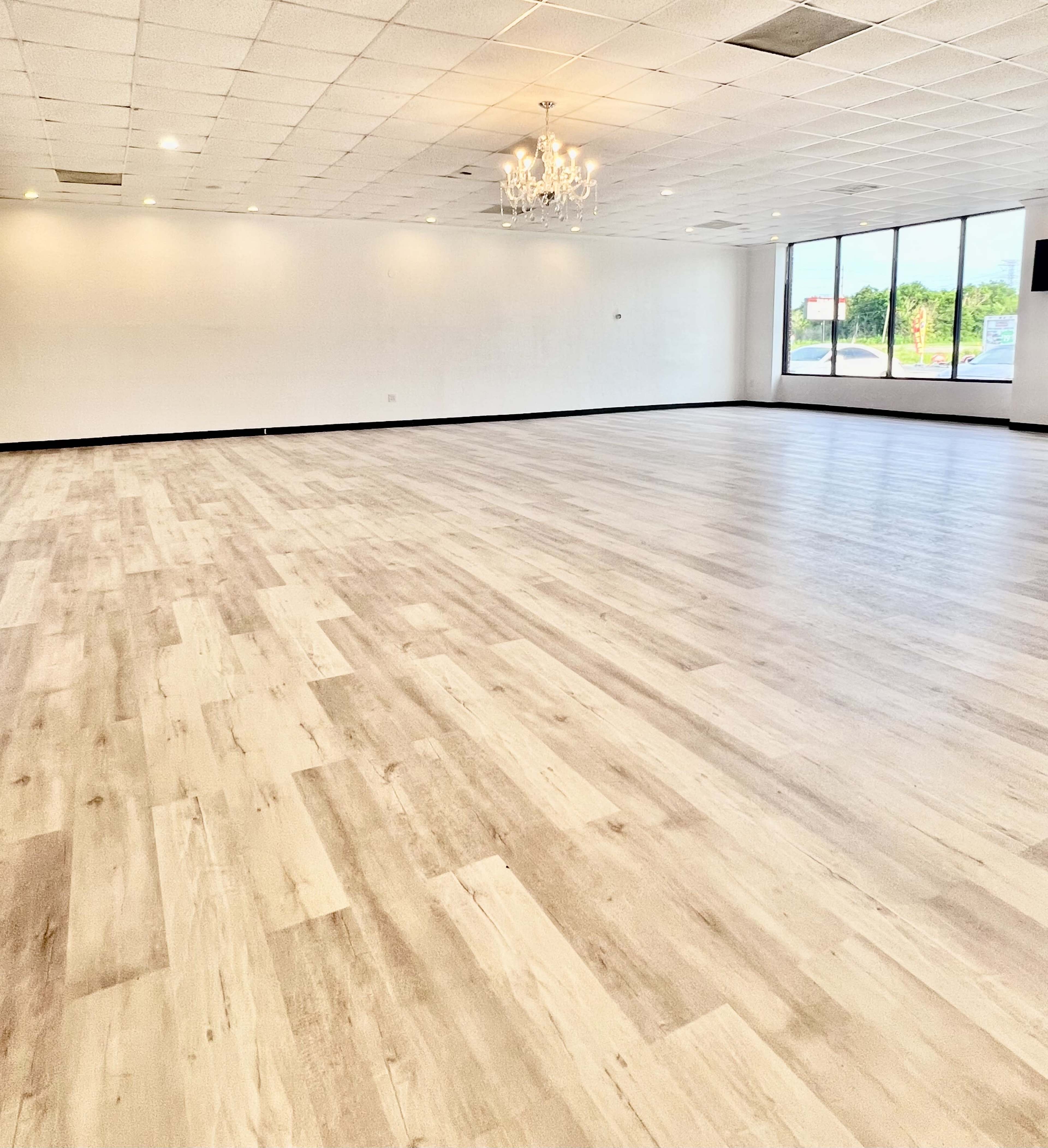 An empty interior space with light-colored wooden flooring and large windows letting in natural light.