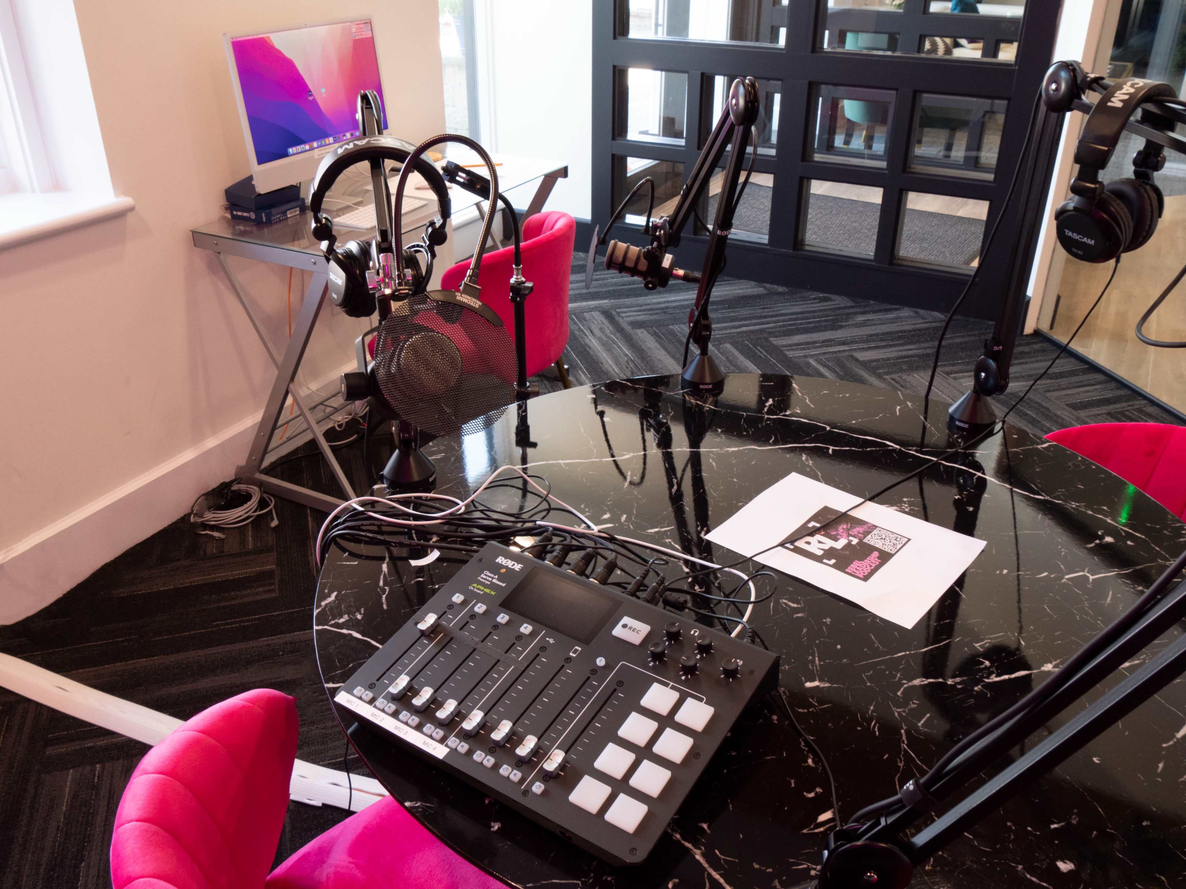 A modern podcasting setup with a round black table, several microphones on adjustable arms, a mixer, and a computer displaying a digital interface.