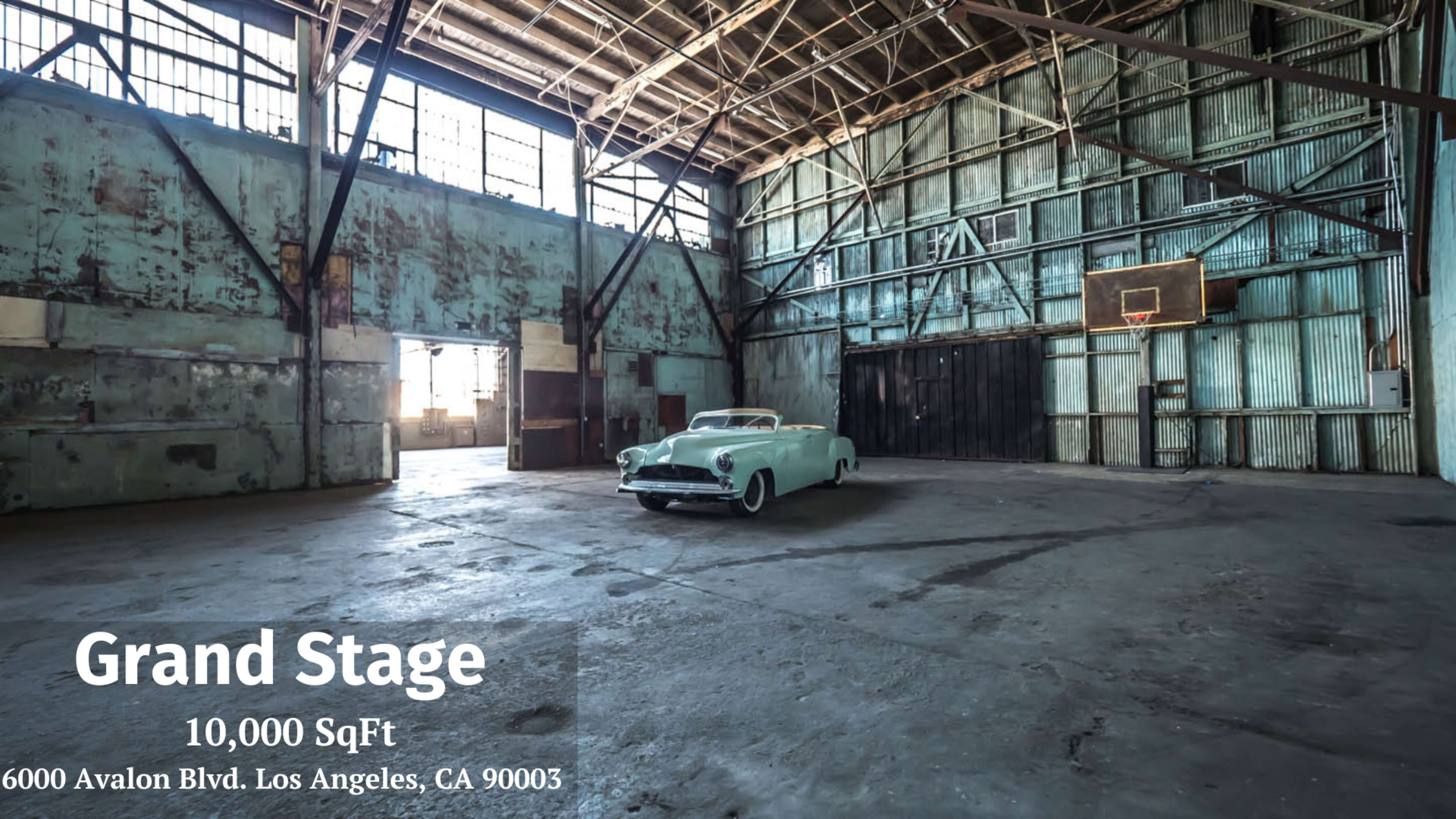 The image shows a spacious, empty warehouse with a vintage car parked in the center, featuring high ceilings and large windows.