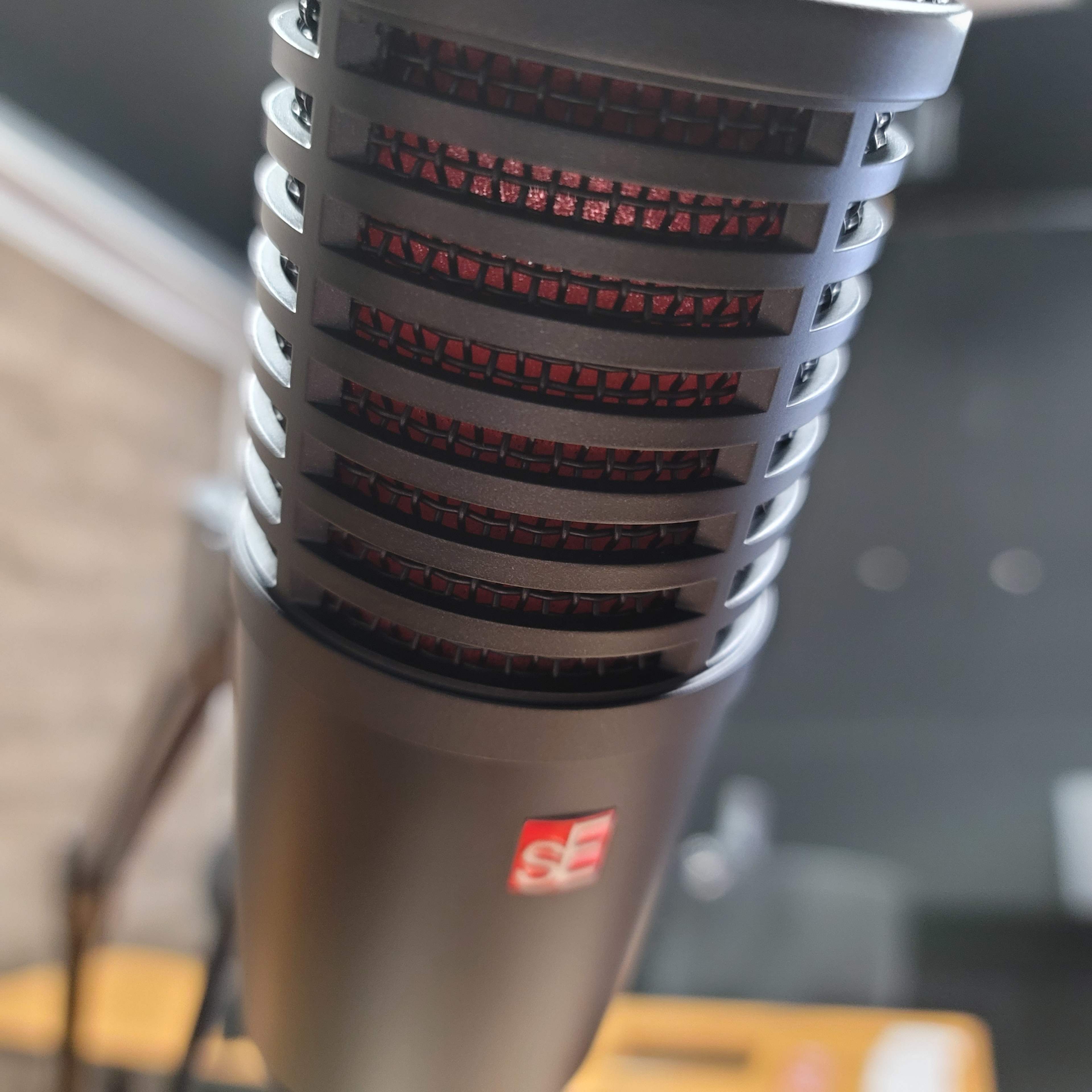 A close-up of a microphone with a black grill and red accents, placed on a wooden surface.