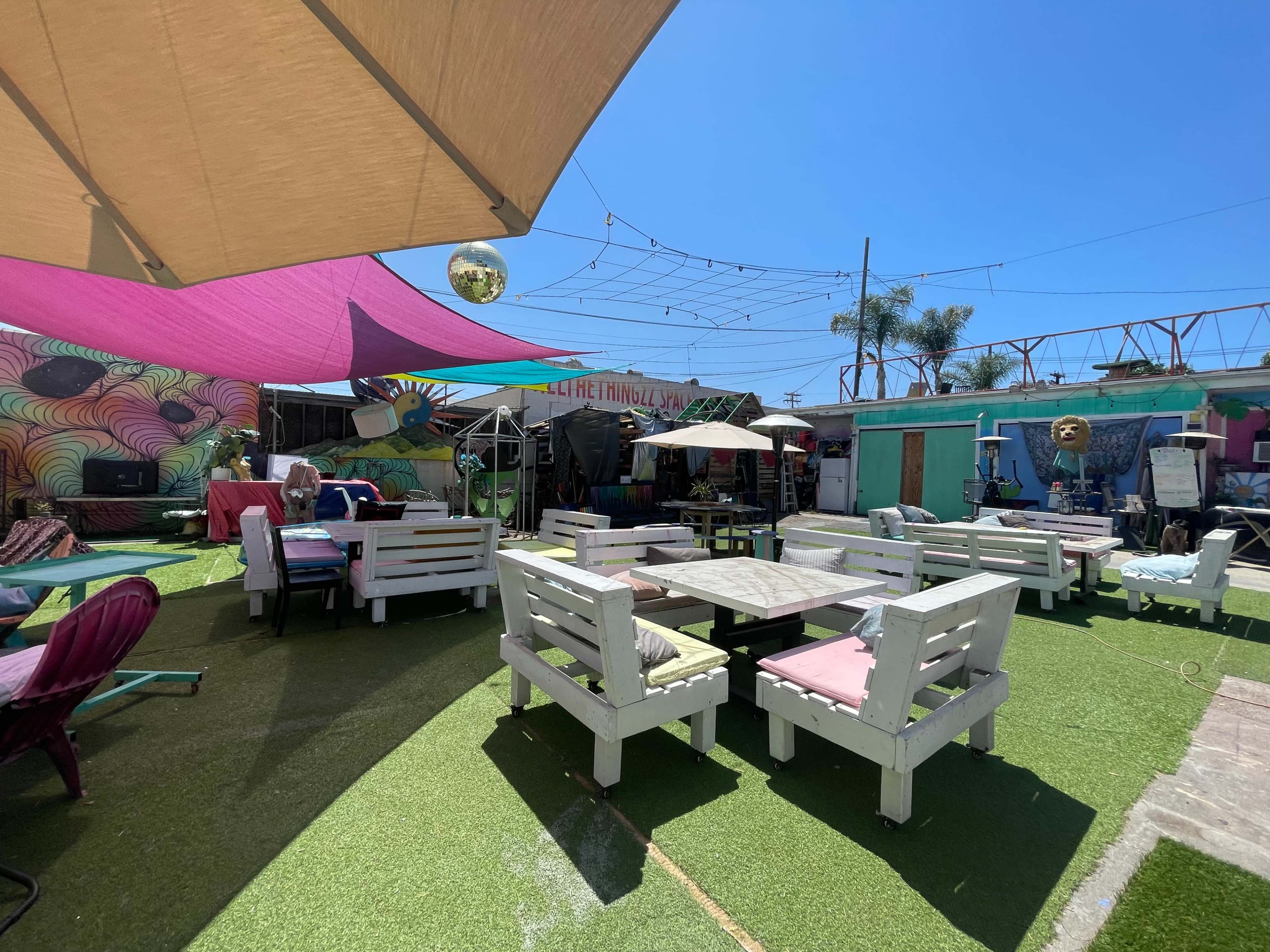 A vibrant outdoor seating area with colorful umbrellas and wooden tables surrounded by decorative murals and greenery.