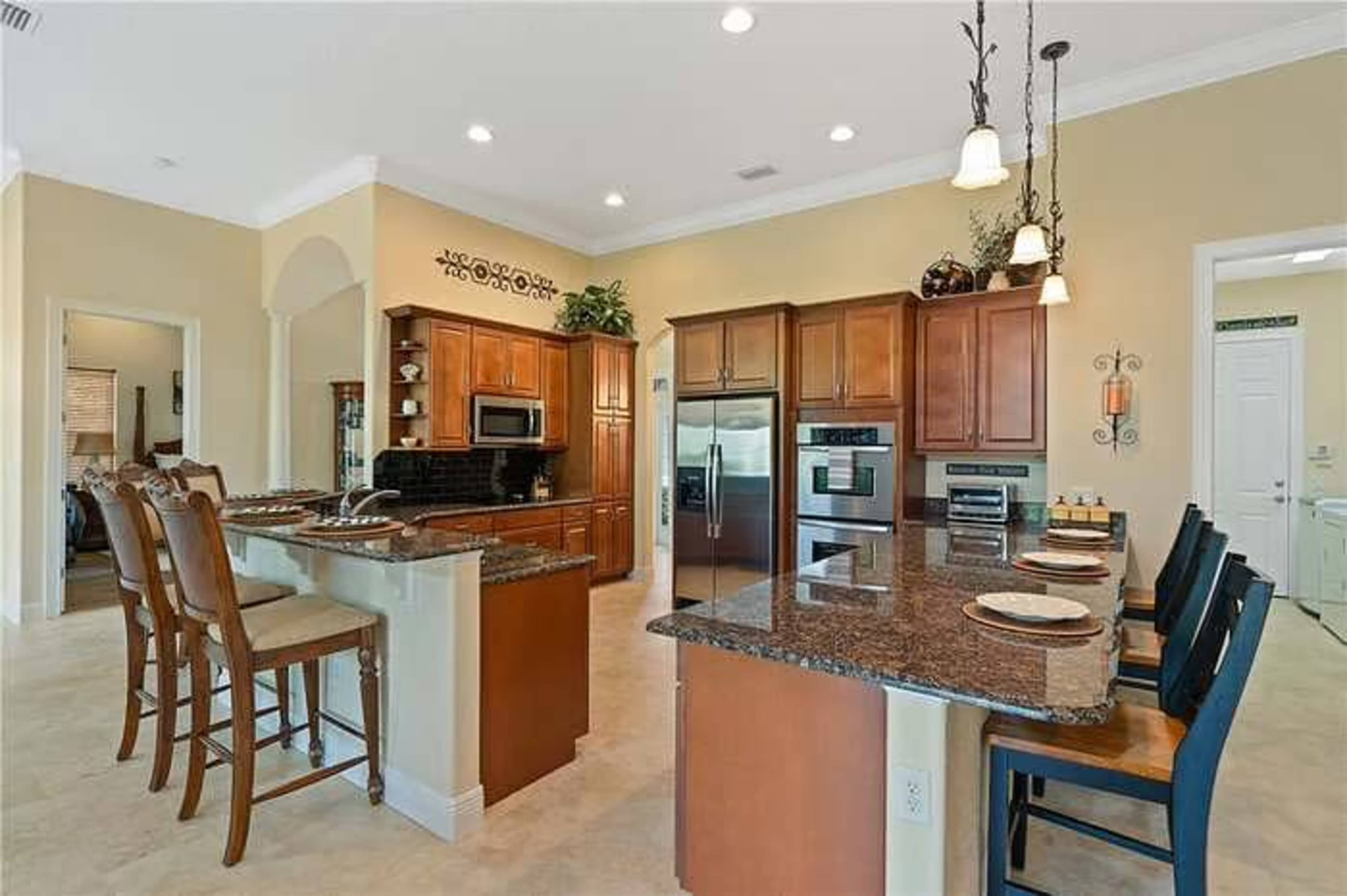 The image shows a spacious kitchen with wooden cabinets, granite countertops, and bar seating for four.