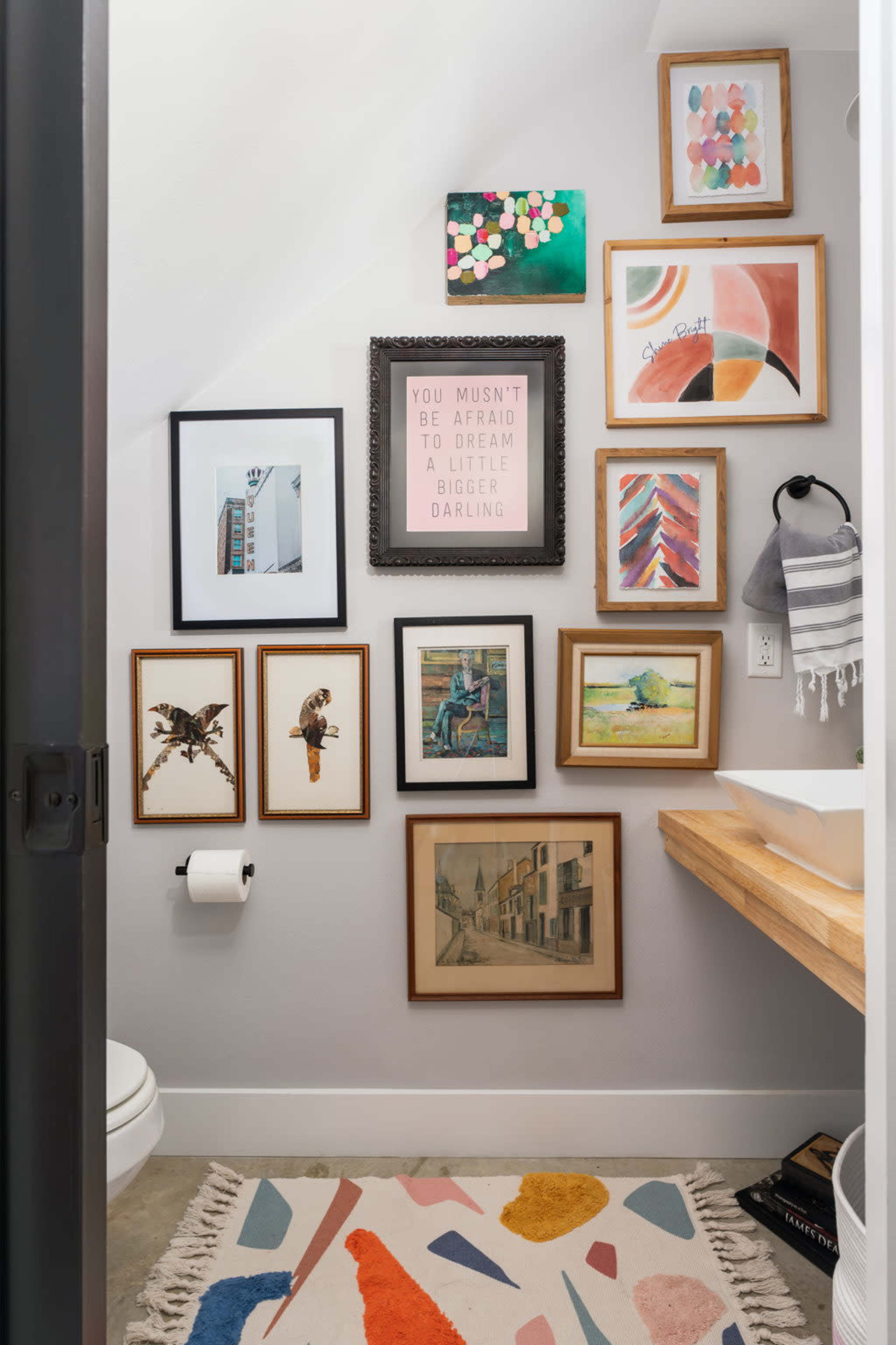 A small bathroom features a variety of framed artwork on the walls and a wooden countertop with a sink.