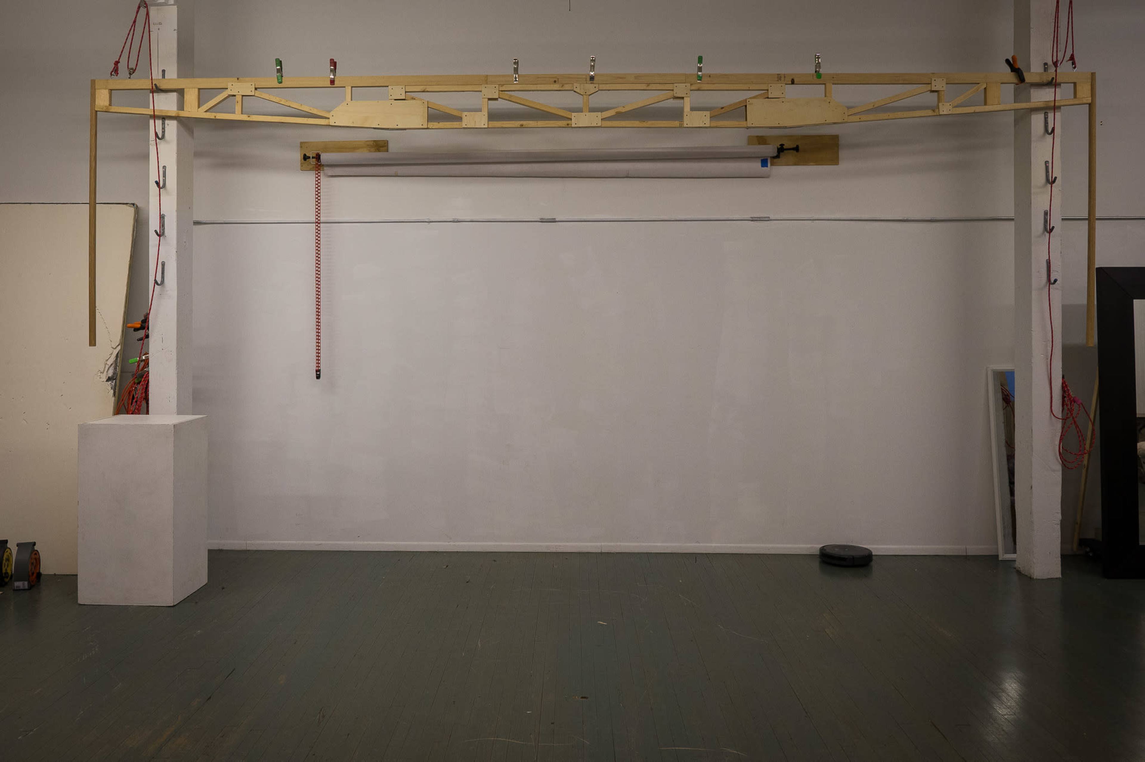 The image shows a large, wooden overhead frame mounted on a wall in an empty room with a wooden floor.