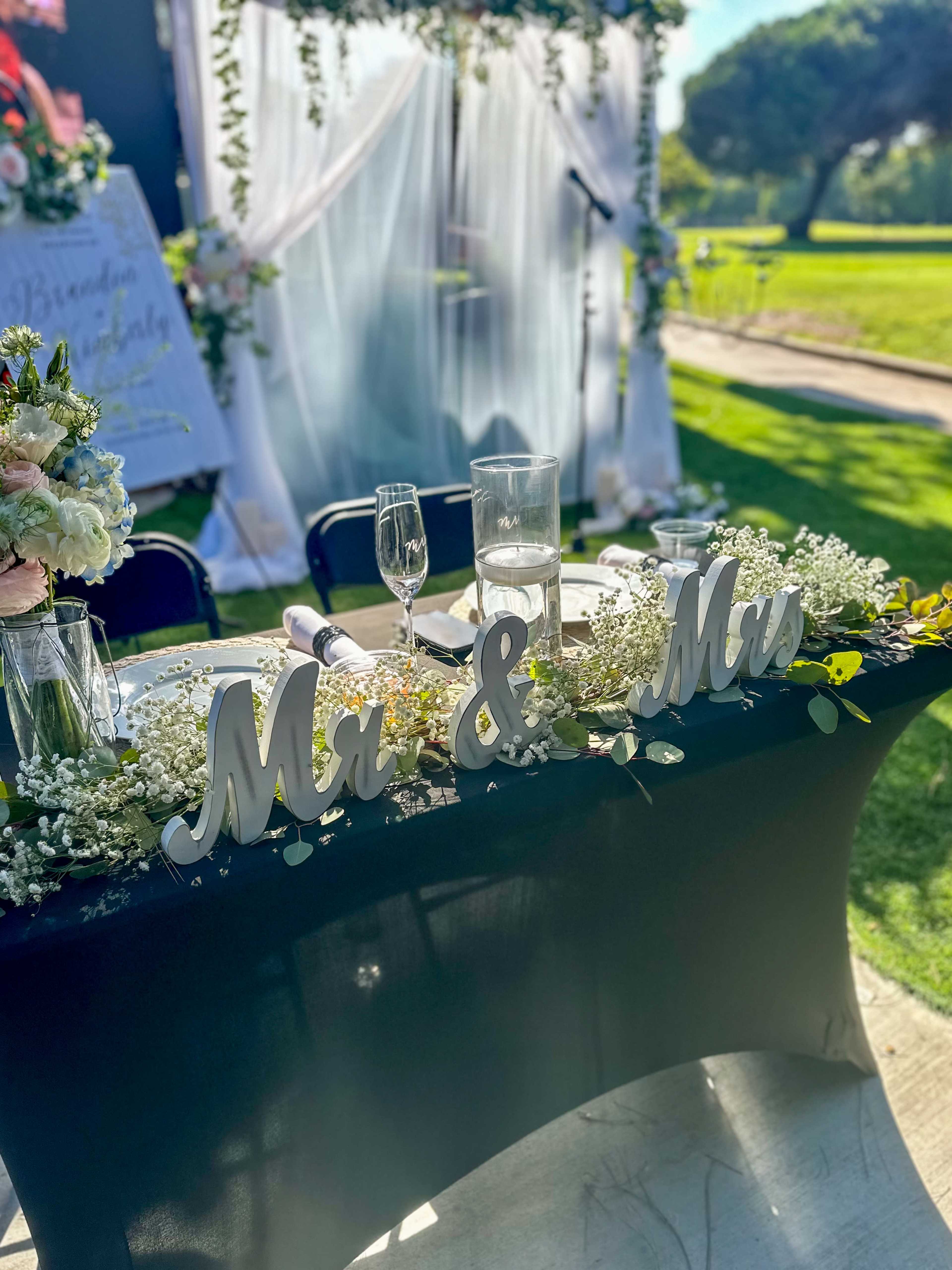 A decorated wedding table features the words "Mr & Mrs" prominently displayed amidst floral arrangements and elegant tableware.