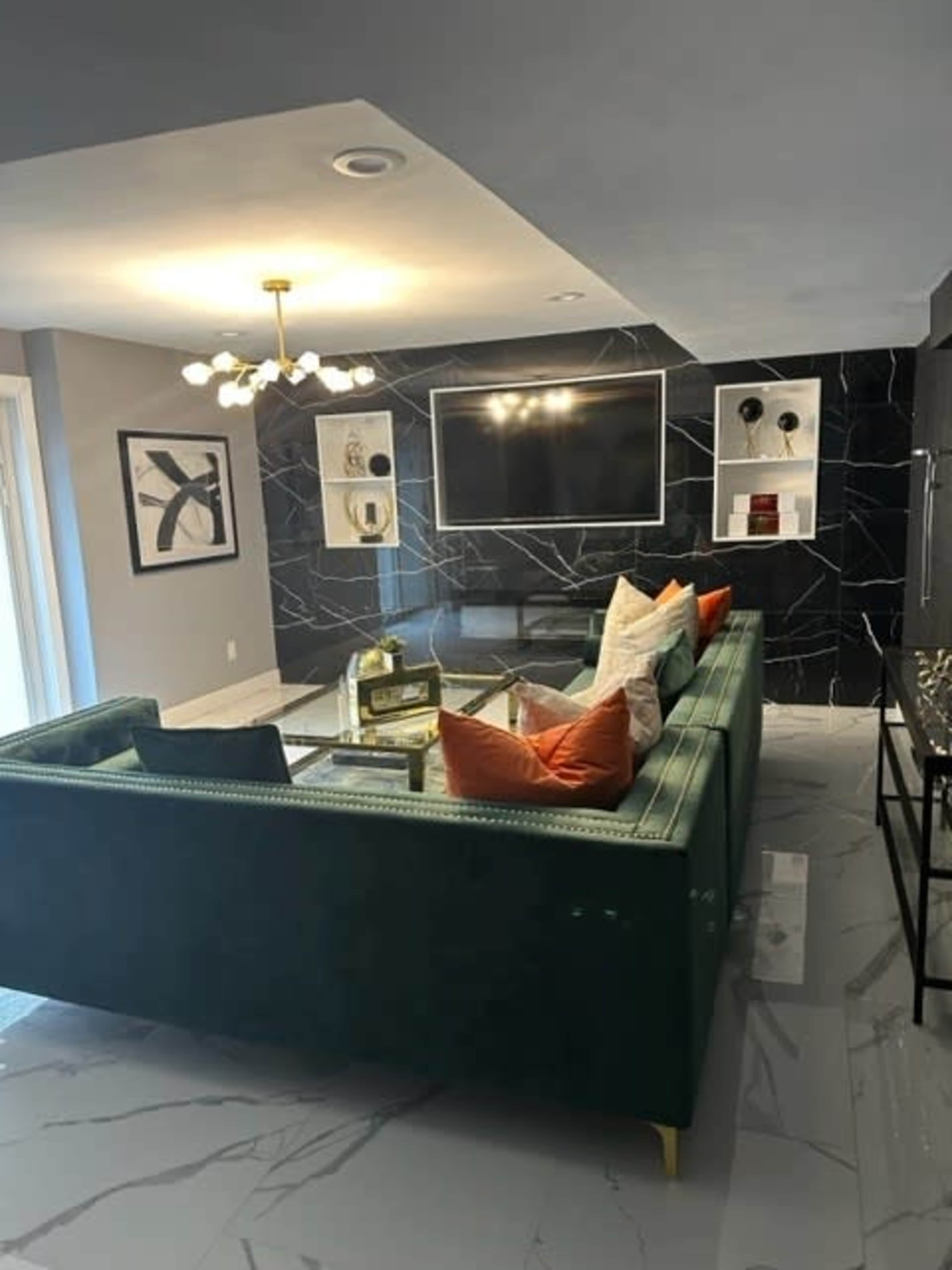 A modern living room featuring a green velvet sofa with colorful pillows, a wall-mounted TV, and a sleek marble floor.