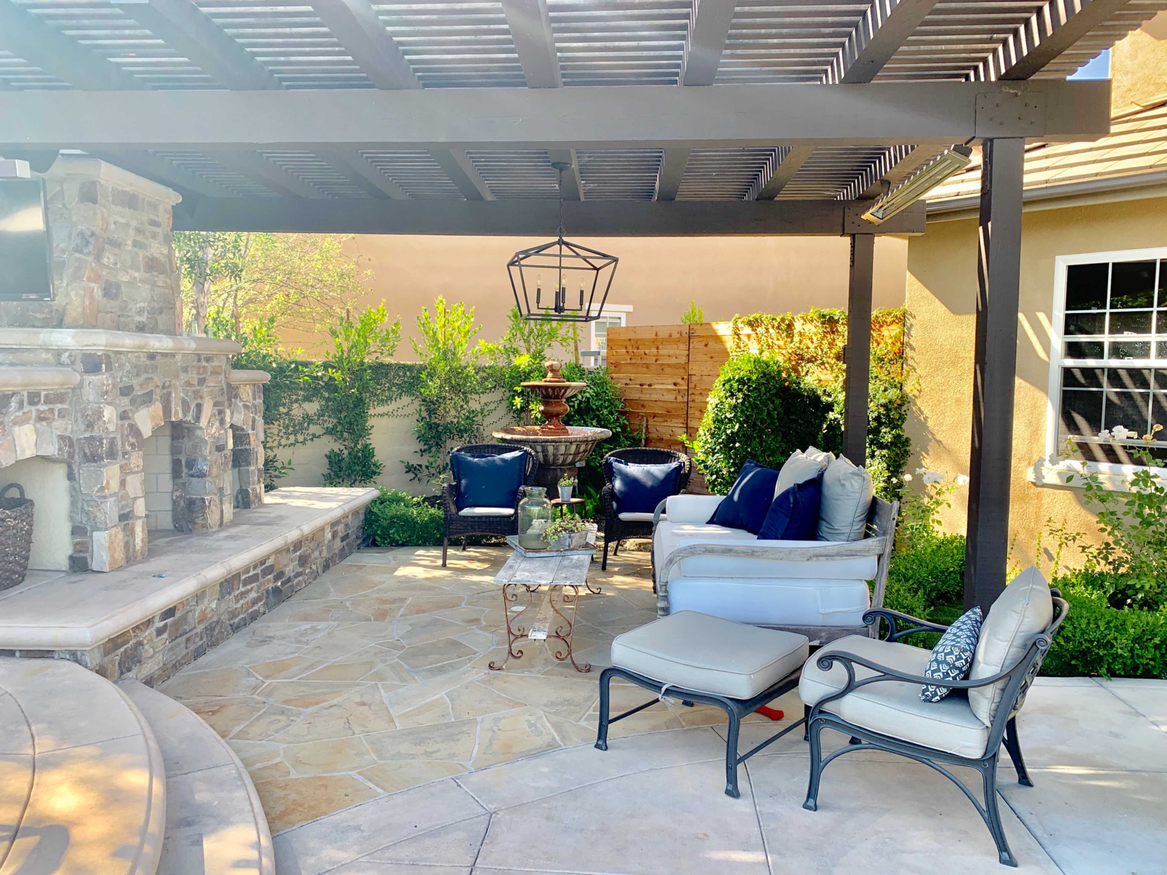 A shaded patio area featuring comfortable seating, a stone fireplace, and decorative plants.