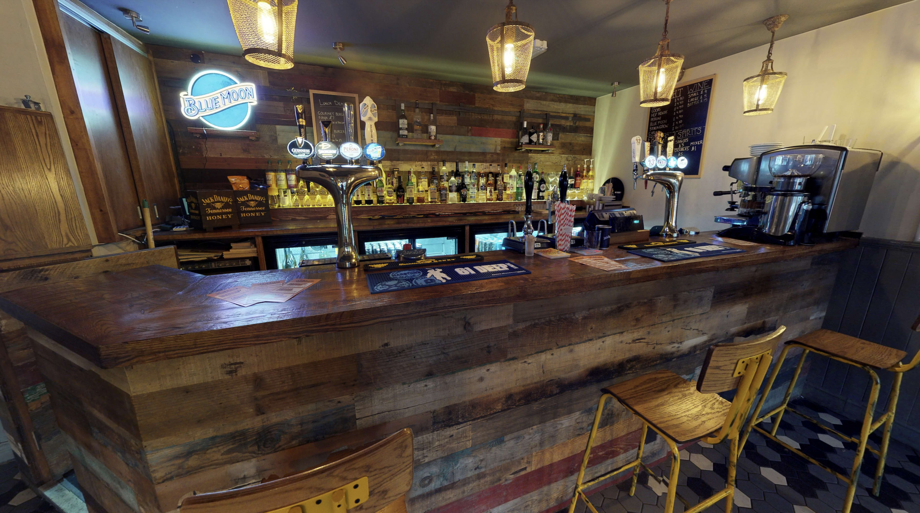 A wooden bar with beer taps, illuminated by pendant lights, and surrounded by high stools.