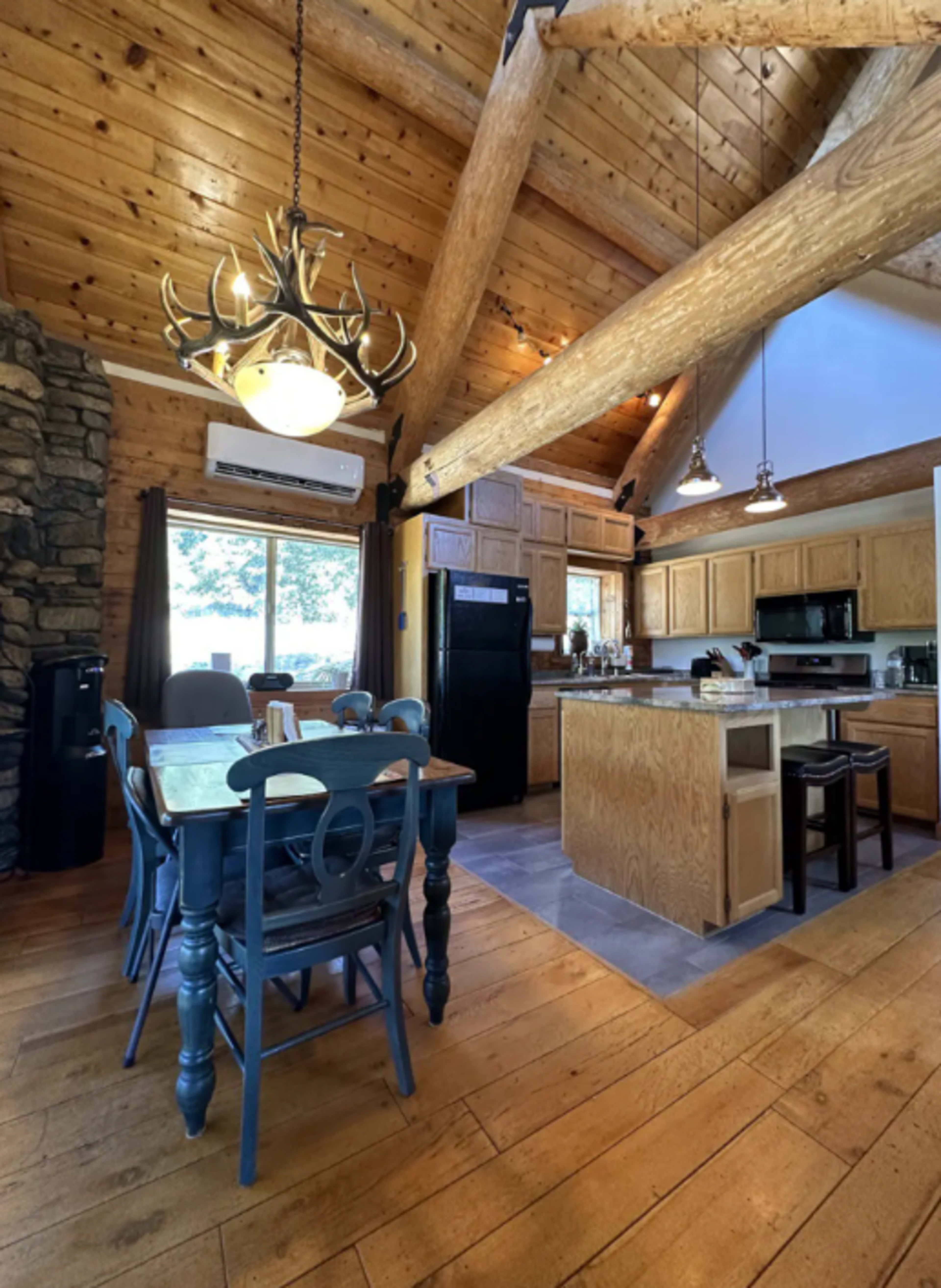 A wooden cabin-style kitchen with a large dining table, a stone accent wall, and exposed beams in the ceiling.