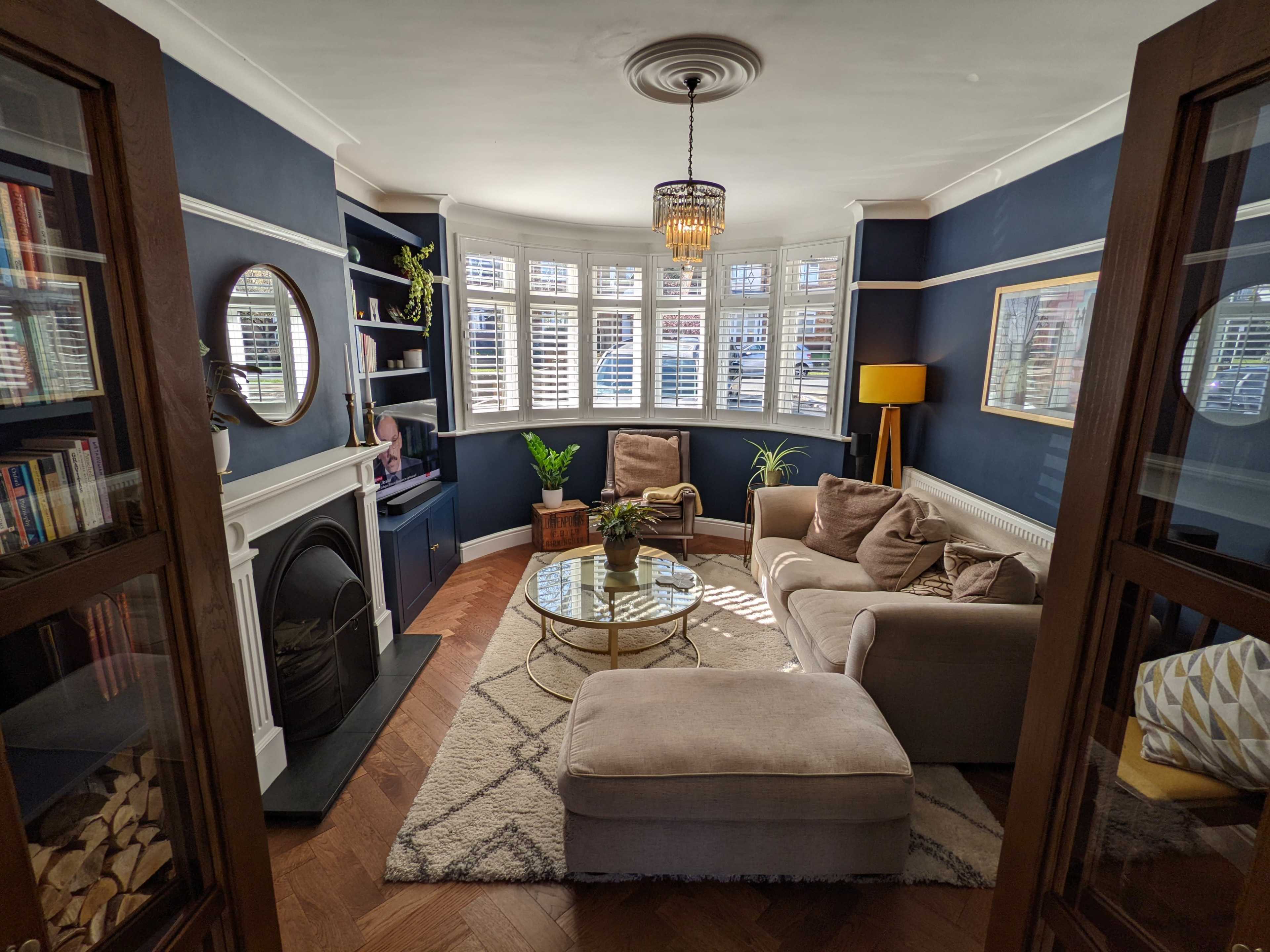 A cozy living room features a circular coffee table, two armchairs, and a decorative lamp, with large windows allowing natural light to illuminate the space.