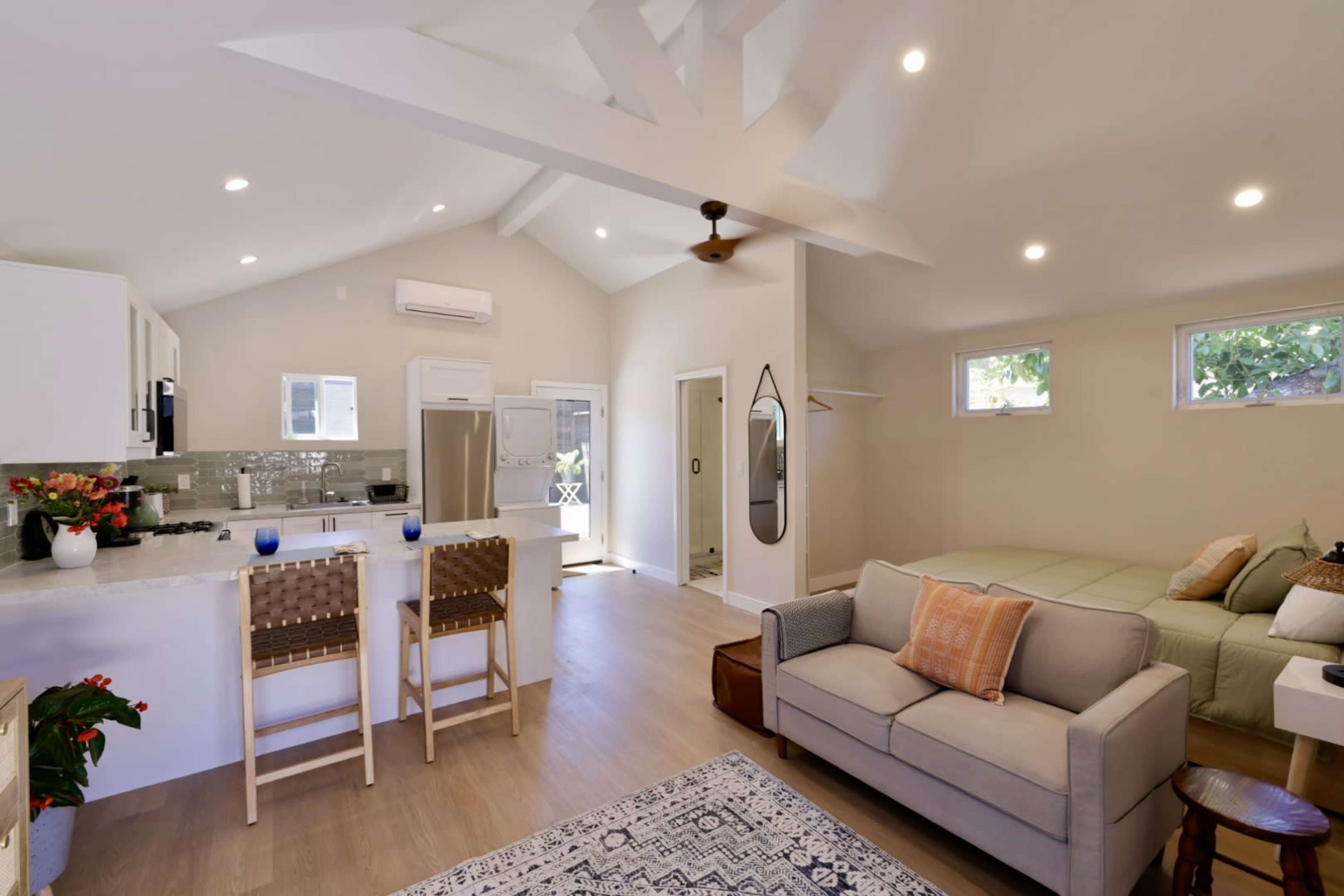 A modern, open-concept living space with a kitchen, a seating area, and a bedroom area featuring a large window and sliding doors.