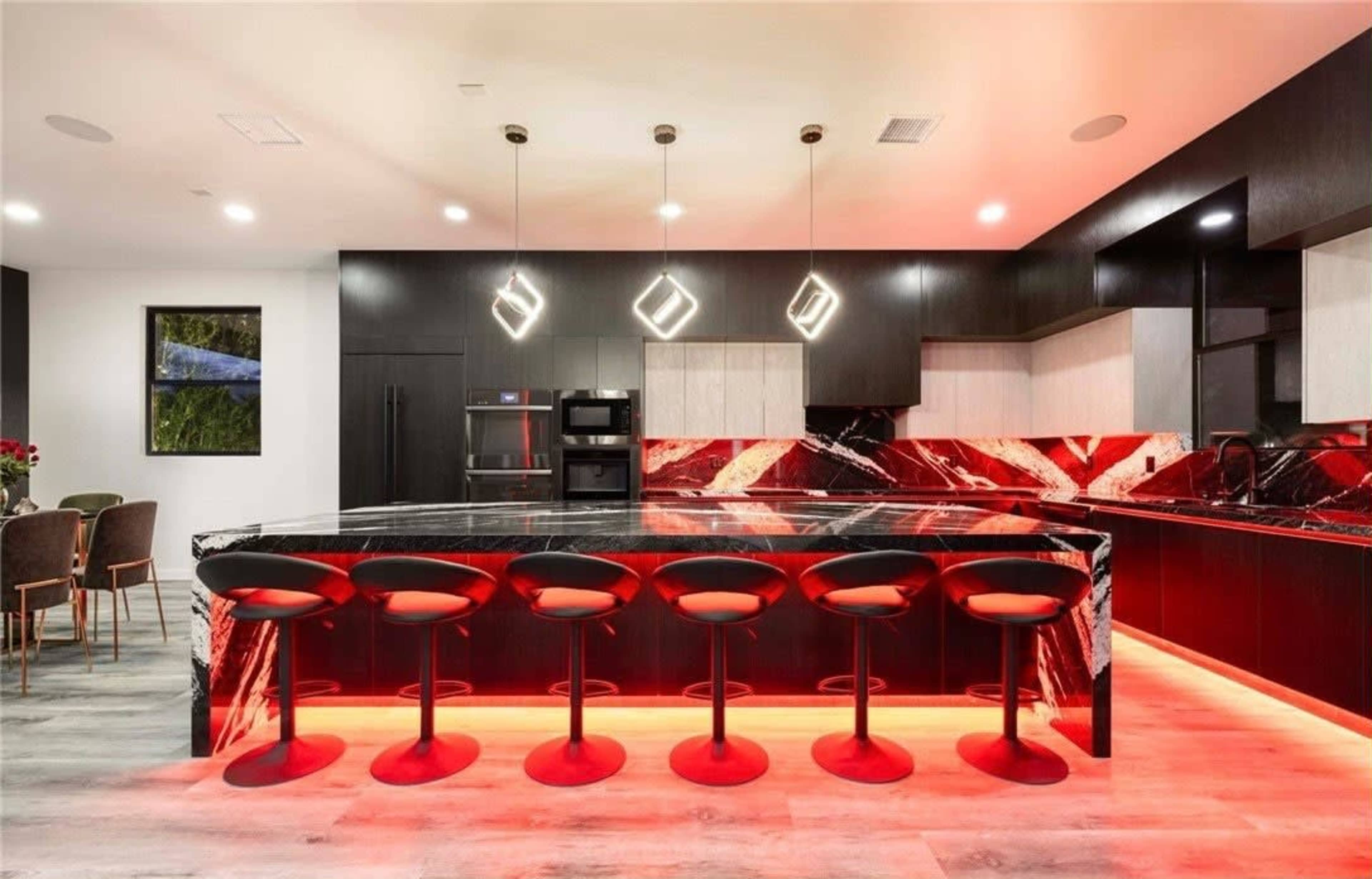 The kitchen features a large, black and red marbled island with seven black bar stools and modern pendant lighting.