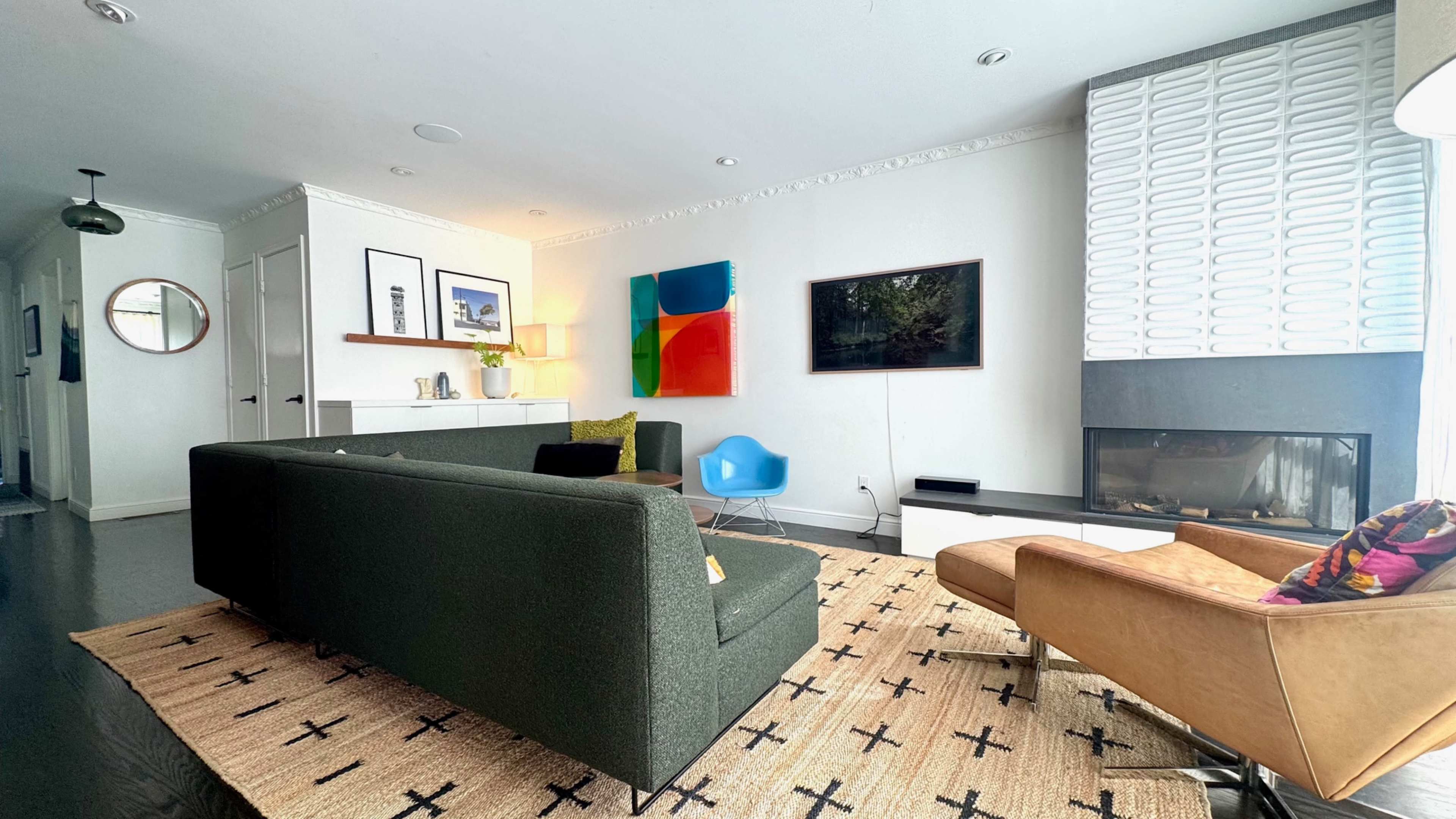 The image depicts a modern living room featuring a green sofa, a tan armchair, a fireplace, and various artworks on the walls.