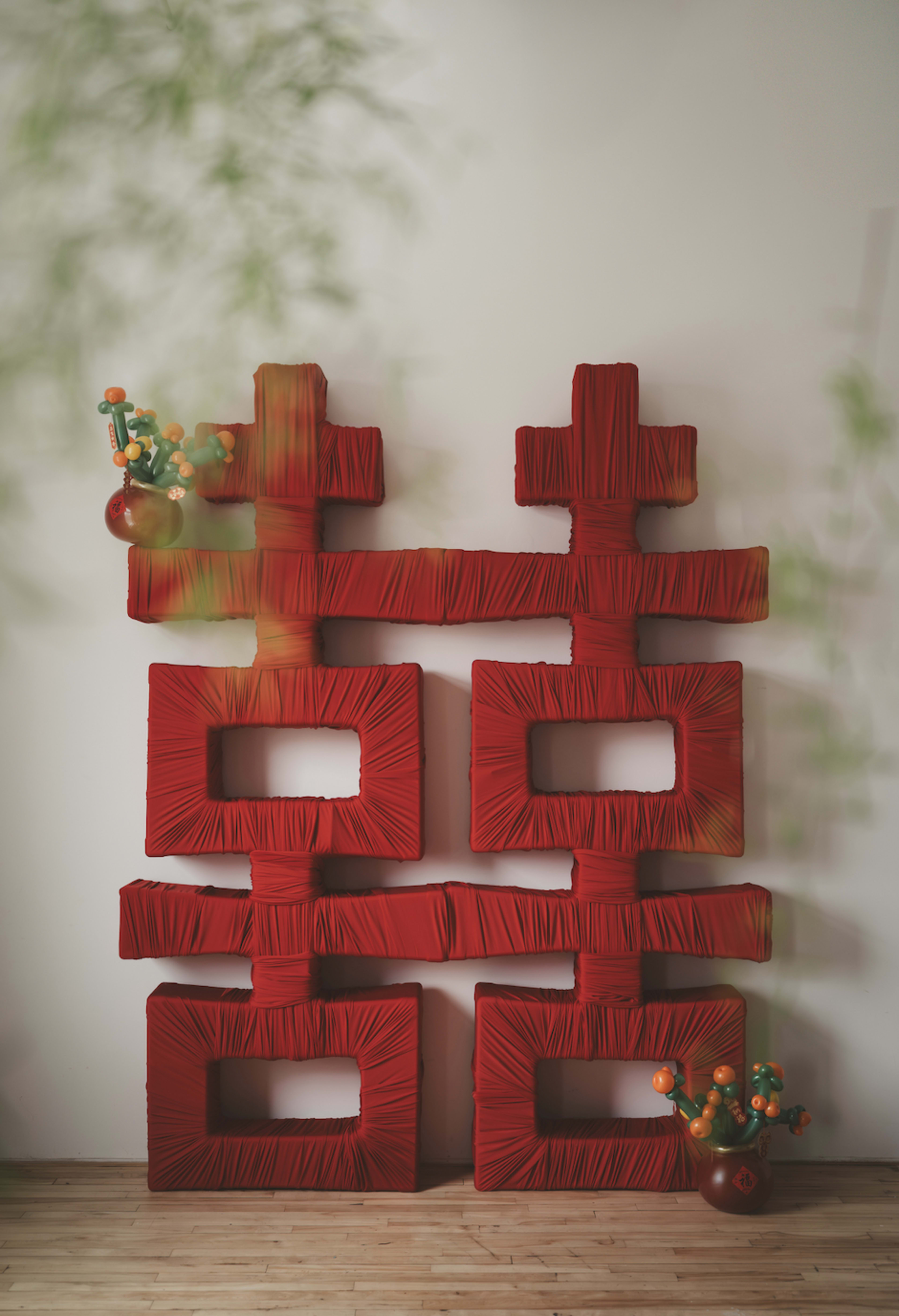 The image features a decorative arrangement of large red fabric-covered squares and rectangles on a wall, accompanied by a vase of colorful artificial flowers.