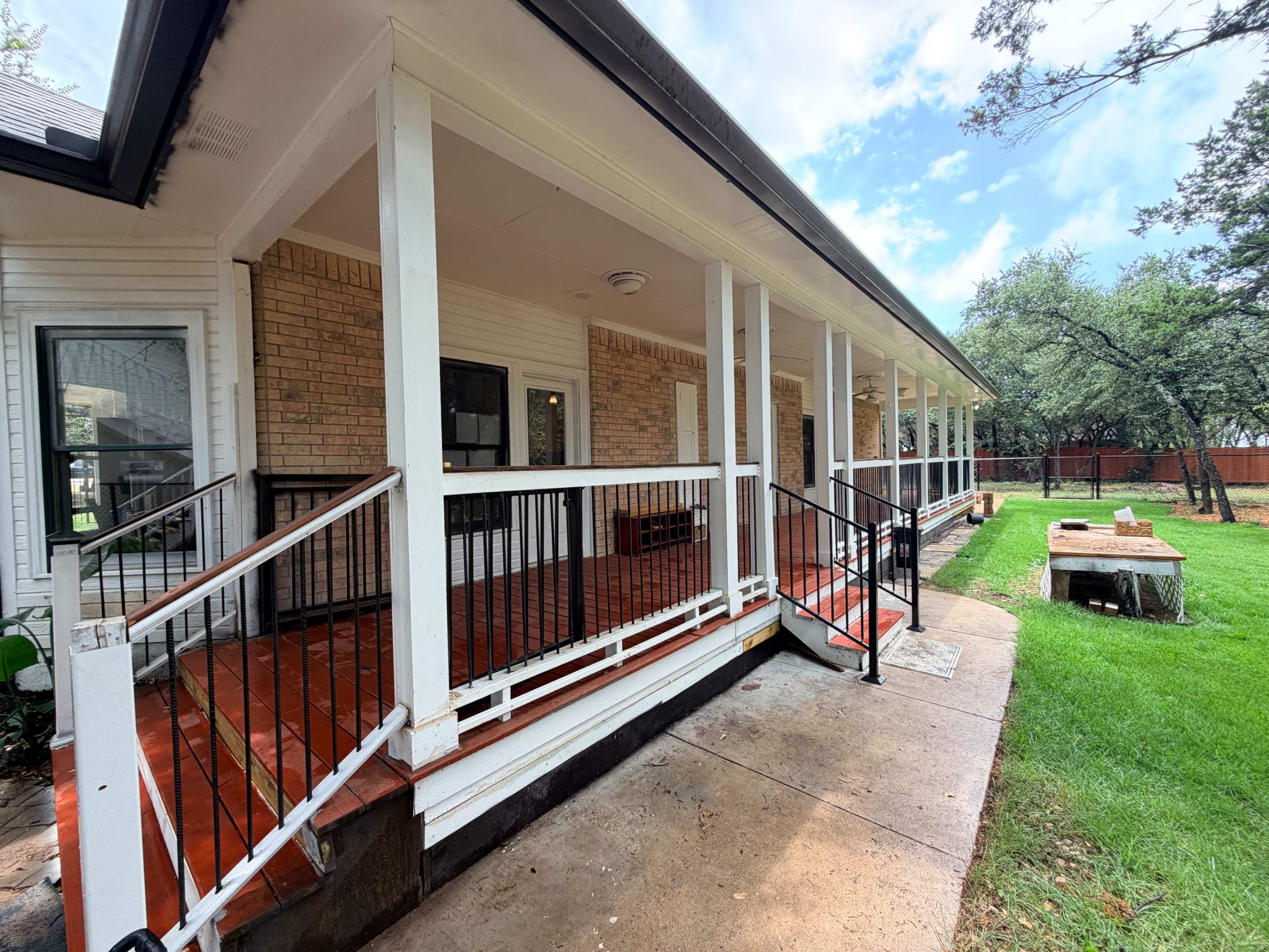 The image shows a single-story house with a covered porch, wooden railing, and a manicured lawn featuring a fire pit area.