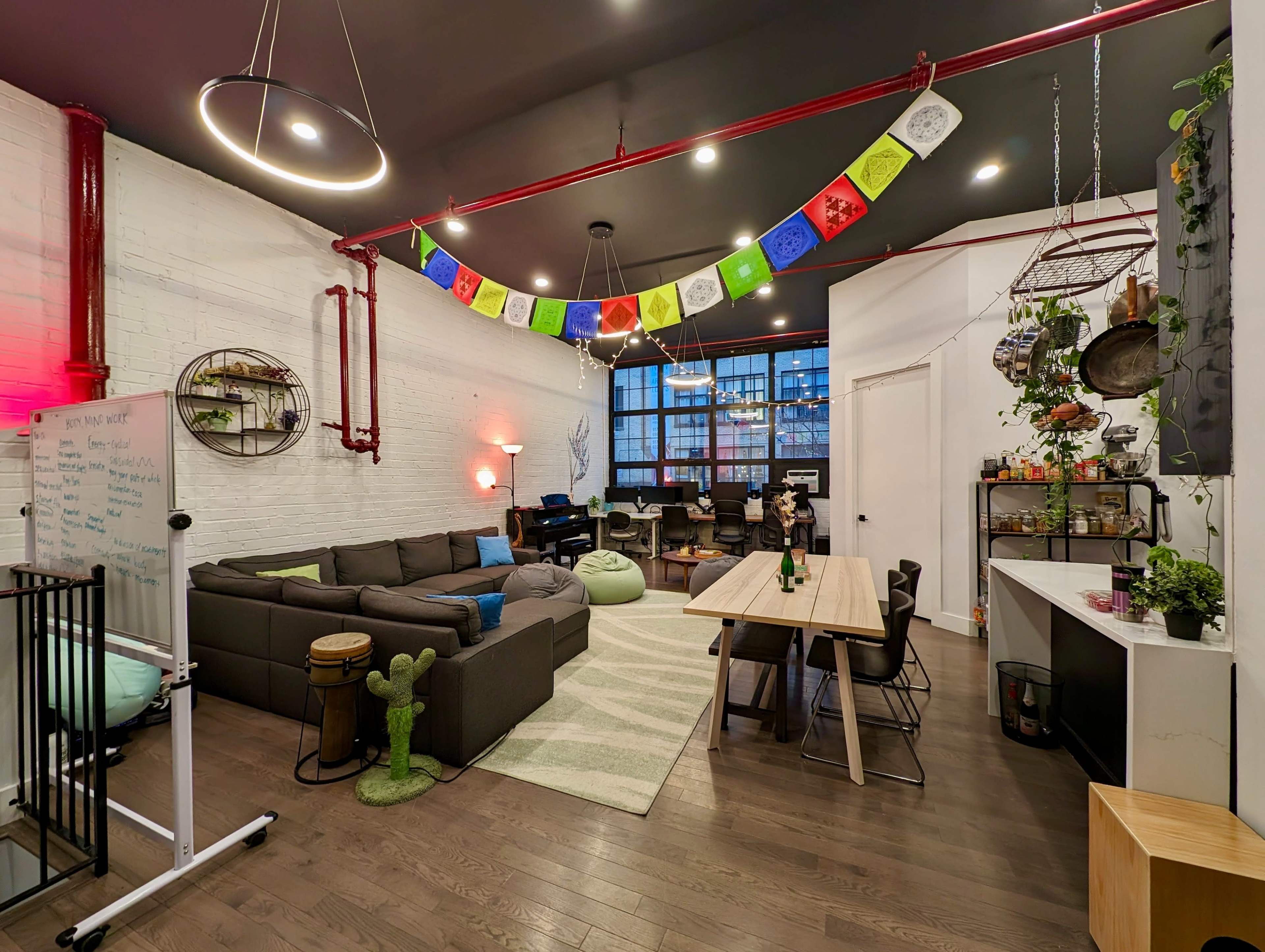 A modern open-plan living space featuring a sectional sofa, a dining table, and colorful decorative elements, with large windows providing natural light.