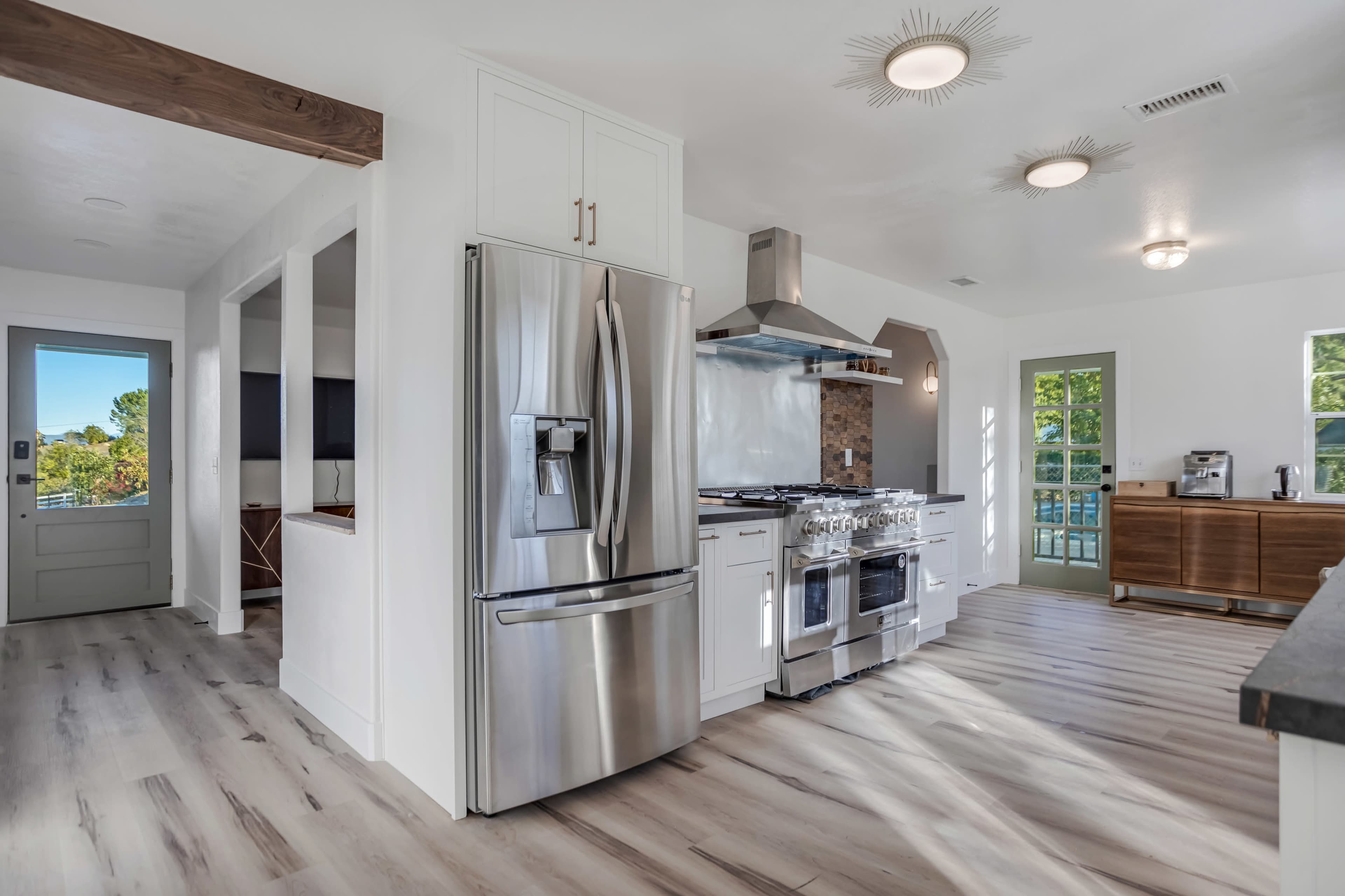 A modern kitchen with stainless steel appliances, including a refrigerator and a gas stove, under bright lighting and wood accents.