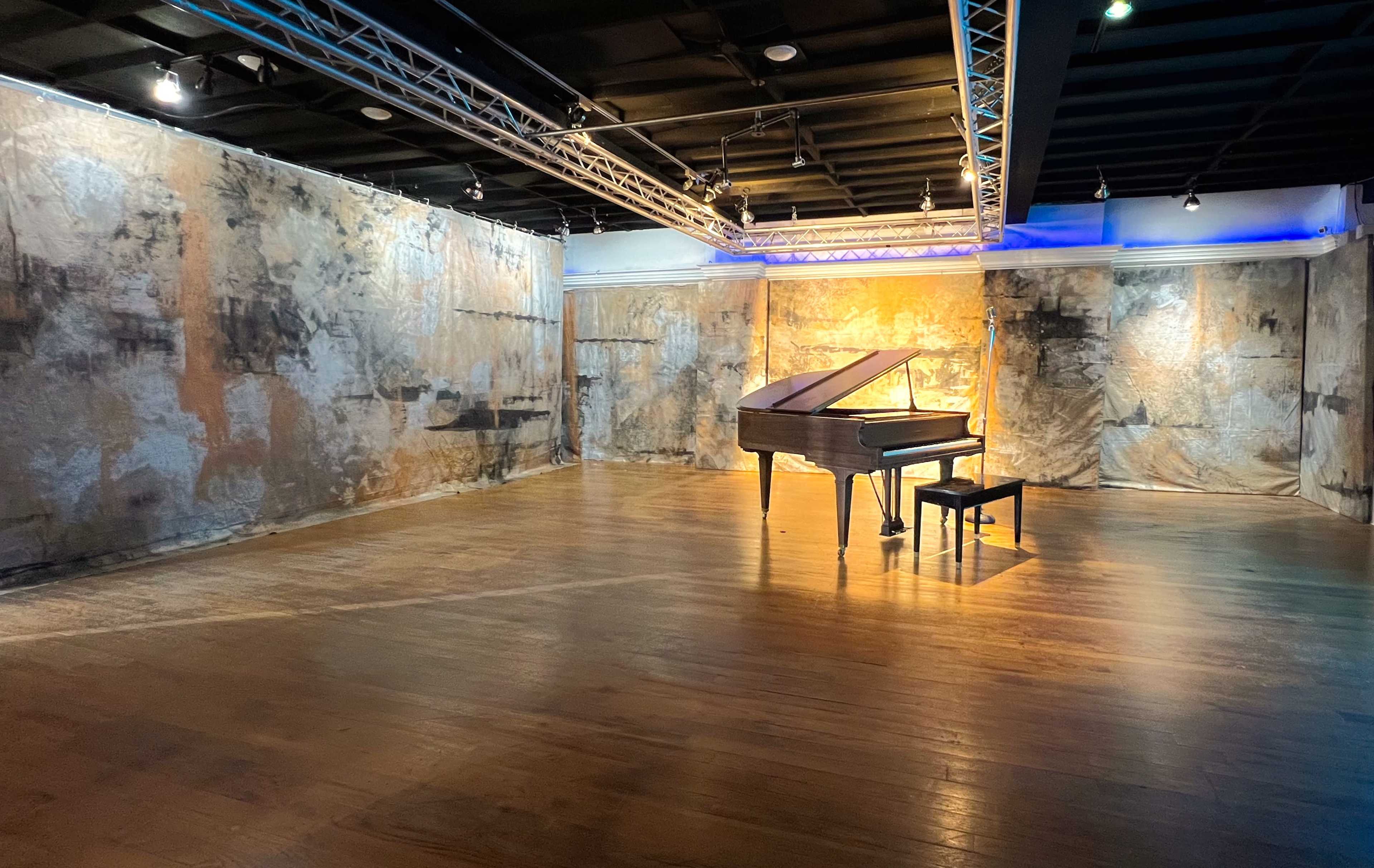 A grand piano sits alone in the center of a spacious room with textured, painted walls and wooden flooring.